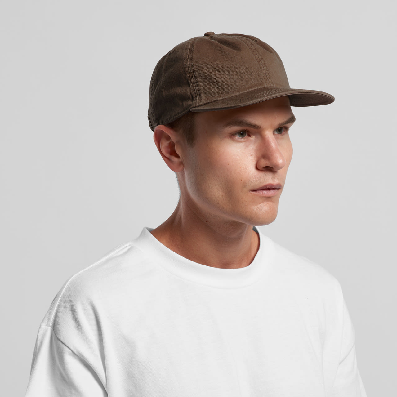A cap in a muted brown colour worn by a model, featuring a simple design and a logo. Class Cap - Image 1