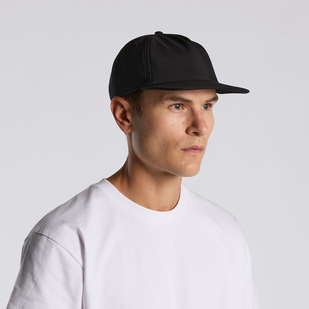 A black cap with a flat brim, worn by a model in a white t-shirt, featuring branding on the front. Class Performance Cap - Image 1