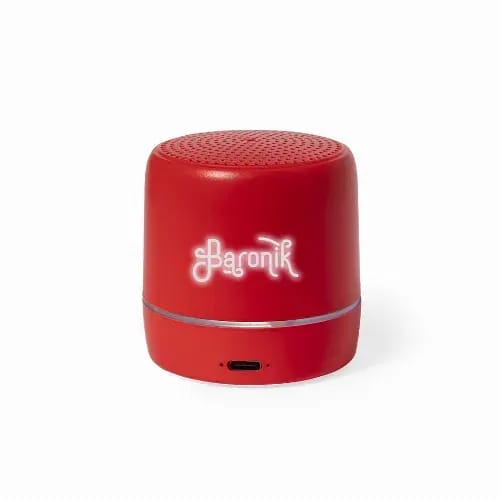 A red portable speaker with a perforated top, featuring a branding logo and a charging port at the base. Kucher - Image 1