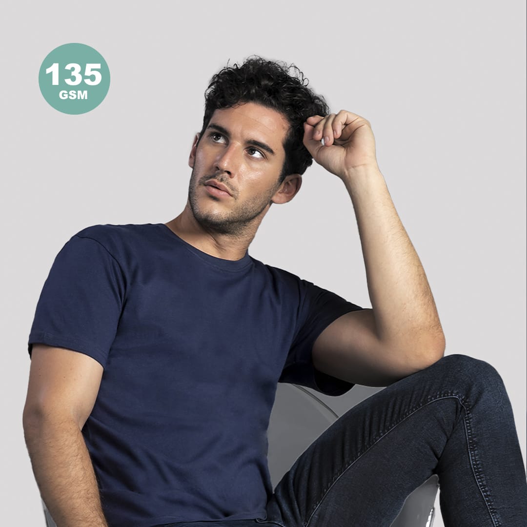 A navy adult colour t-shirt displayed on a seated model, featuring a logo in the corner. Model is wearing jeans. Hecom Adult Colour T-Shirt - Image 1