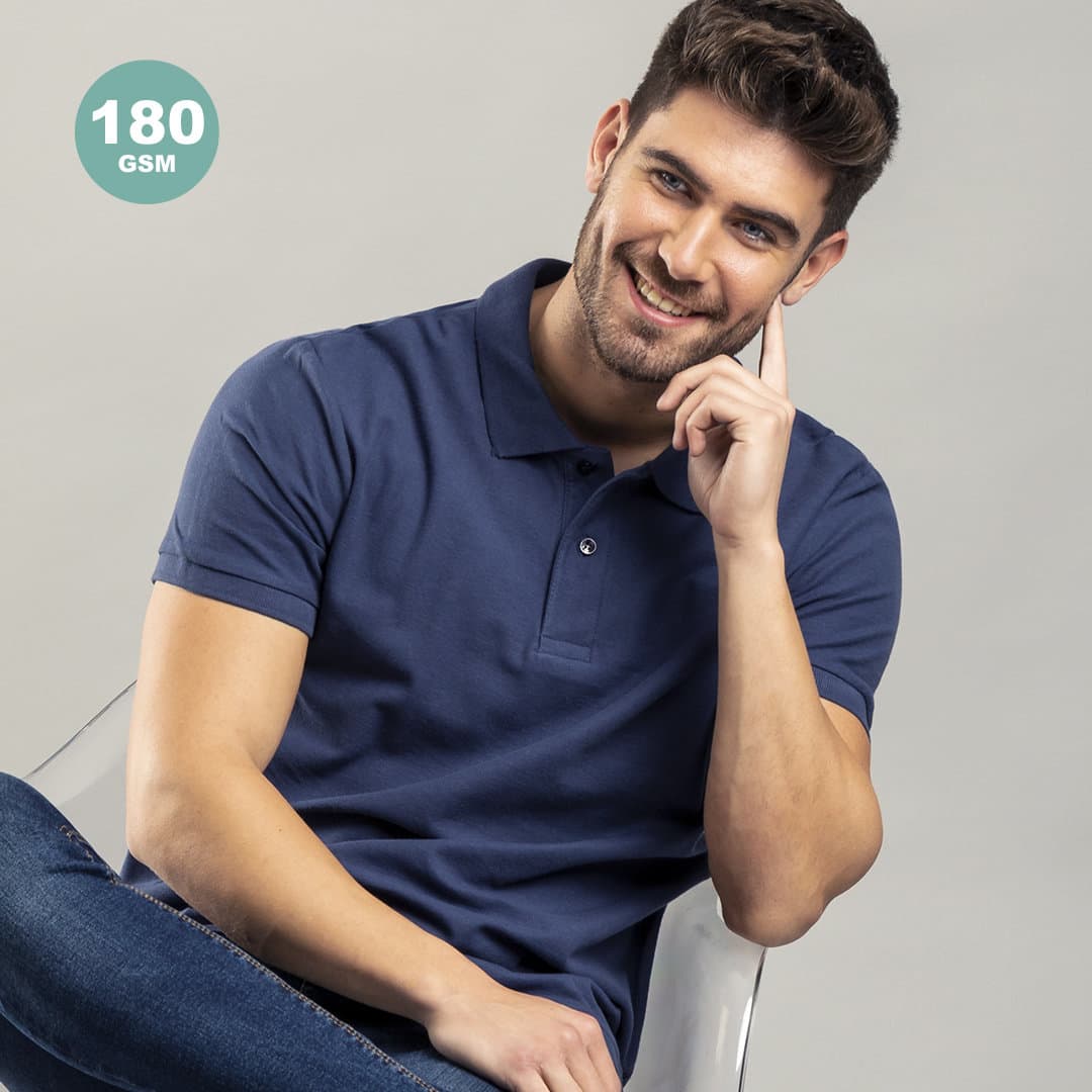 A navy blue polo shirt with a logo, modelled by a smiling man in casual attire, sitting in a chair. Bartel Color Polo Shirt - Image 1