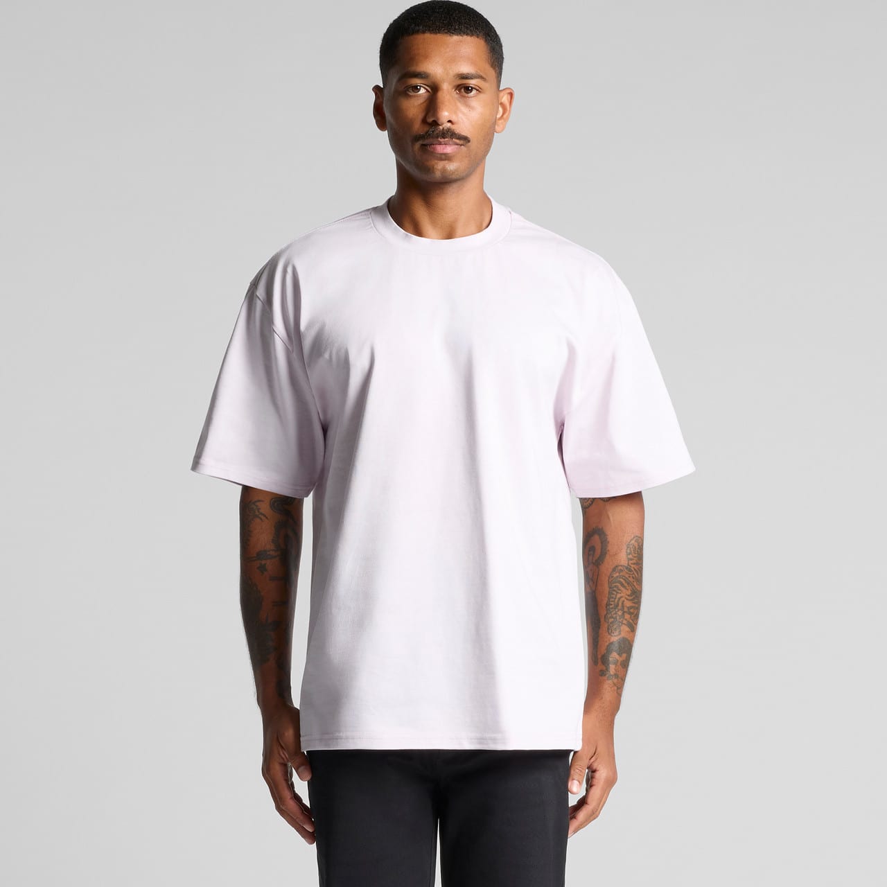 A light pink heavy tee shirt on a person with tattoos, standing against a neutral background. Heavy Tee - Image 1