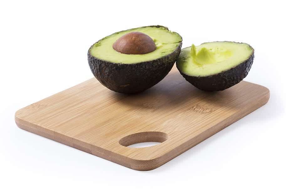A wooden chopping board holds a halved avocado with the pit intact, showcasing its vibrant green flesh. Ruban - Image 1