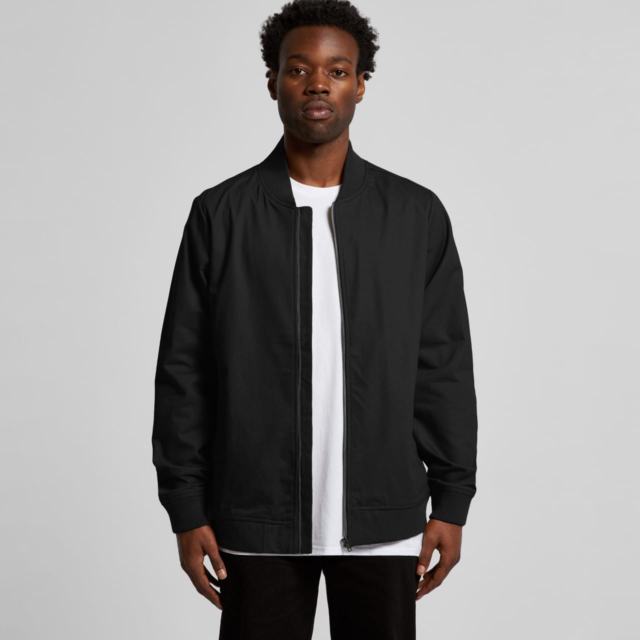 A black bomber jacket worn by a model, featuring a zip front and ribbed cuffs, with a logo visible. Bomber Jacket - Image 1