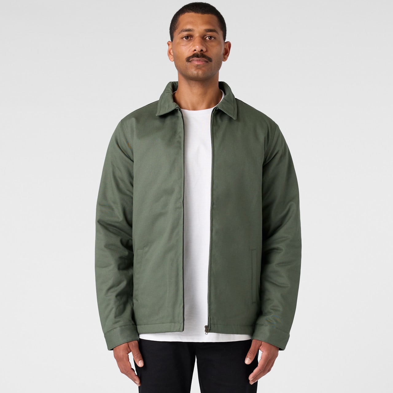 A green service jacket with a collared neck and a zip front, worn over a white t-shirt, displayed against a neutral background. Service Jacket - Image 1