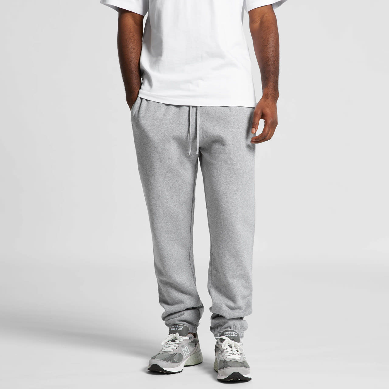 Grey track pants with elastic cuffs and a drawstring waist, worn with a white t-shirt and sneakers. Features a logo. Surplus Track Pants - Image 1