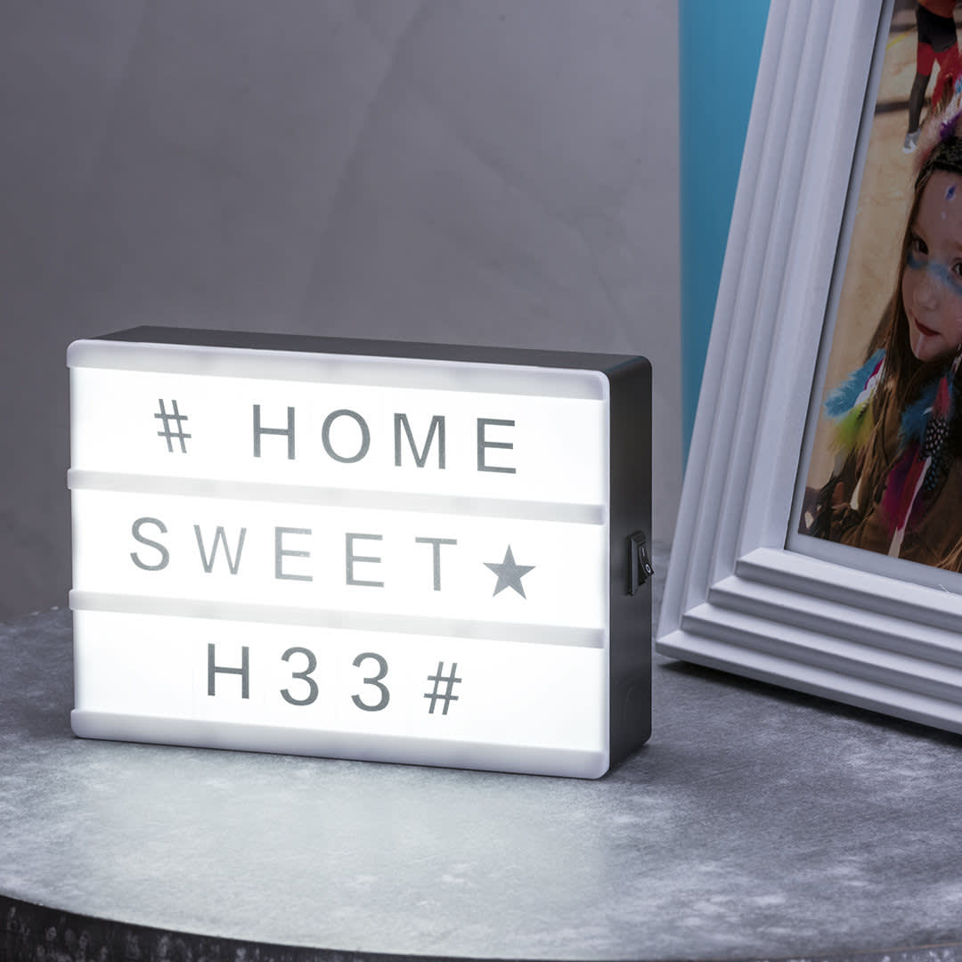 A rectangular light box with a black frame and white panels, displaying letters and symbols, on a grey surface. Cinemax Light Box - Image 1