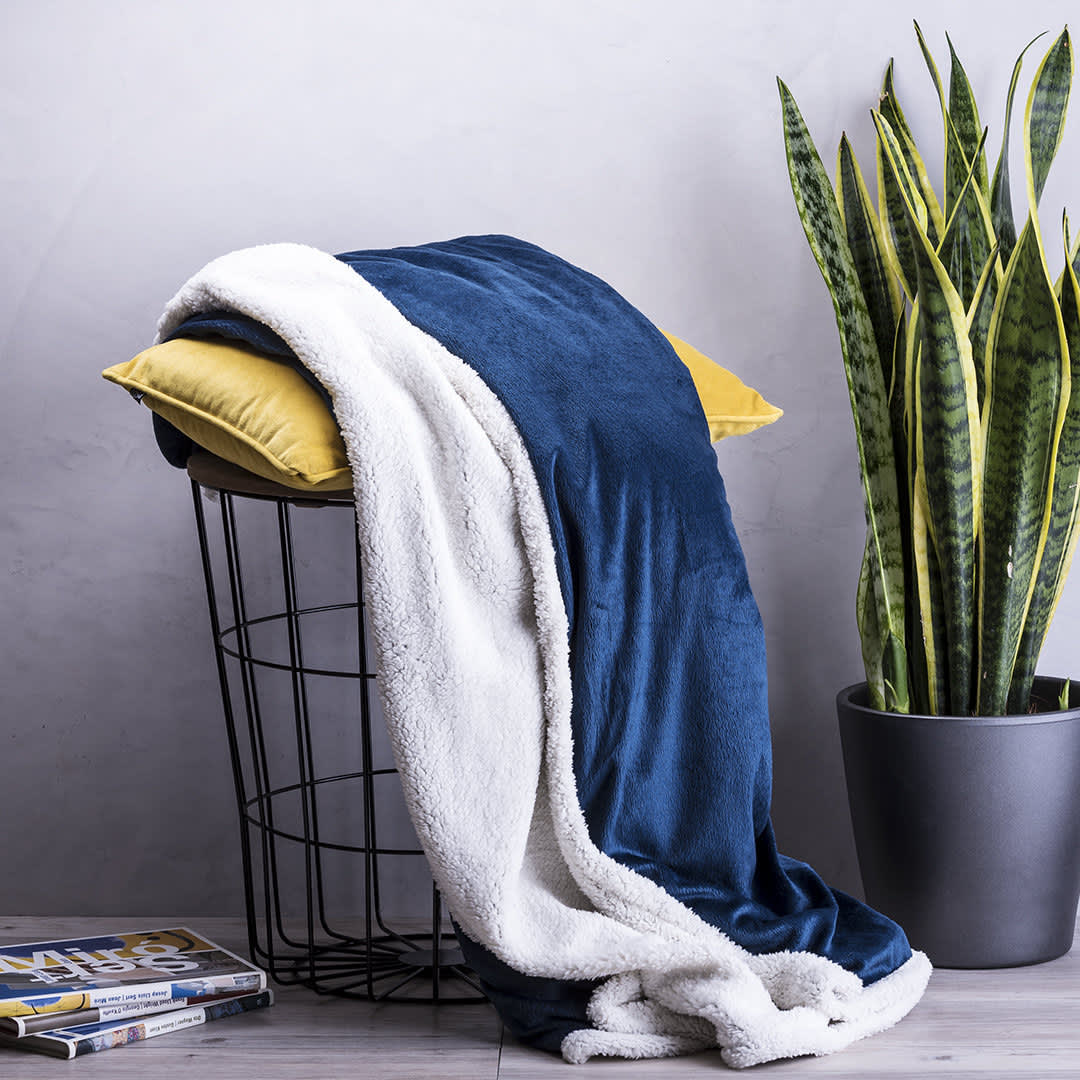 A soft navy blue and white blanket draped over a wire basket, next to a tall green plant in a black pot. Lerten - Image 1