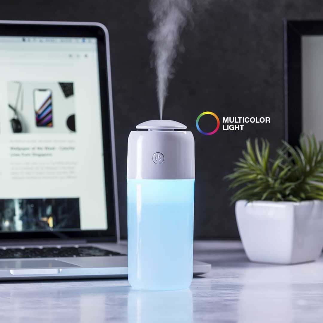 A white and blue humidifier with a multicoloured light feature sits beside a laptop on a desk. Trudy Humidifier - Image 1