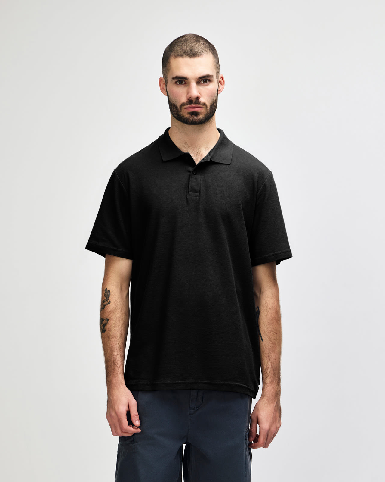 A model wearing a black Gildan Softstyle Adult Double Pique Polo with a logo on the chest. Gildan Softstyle Adult Double Pique Polo - Image 1