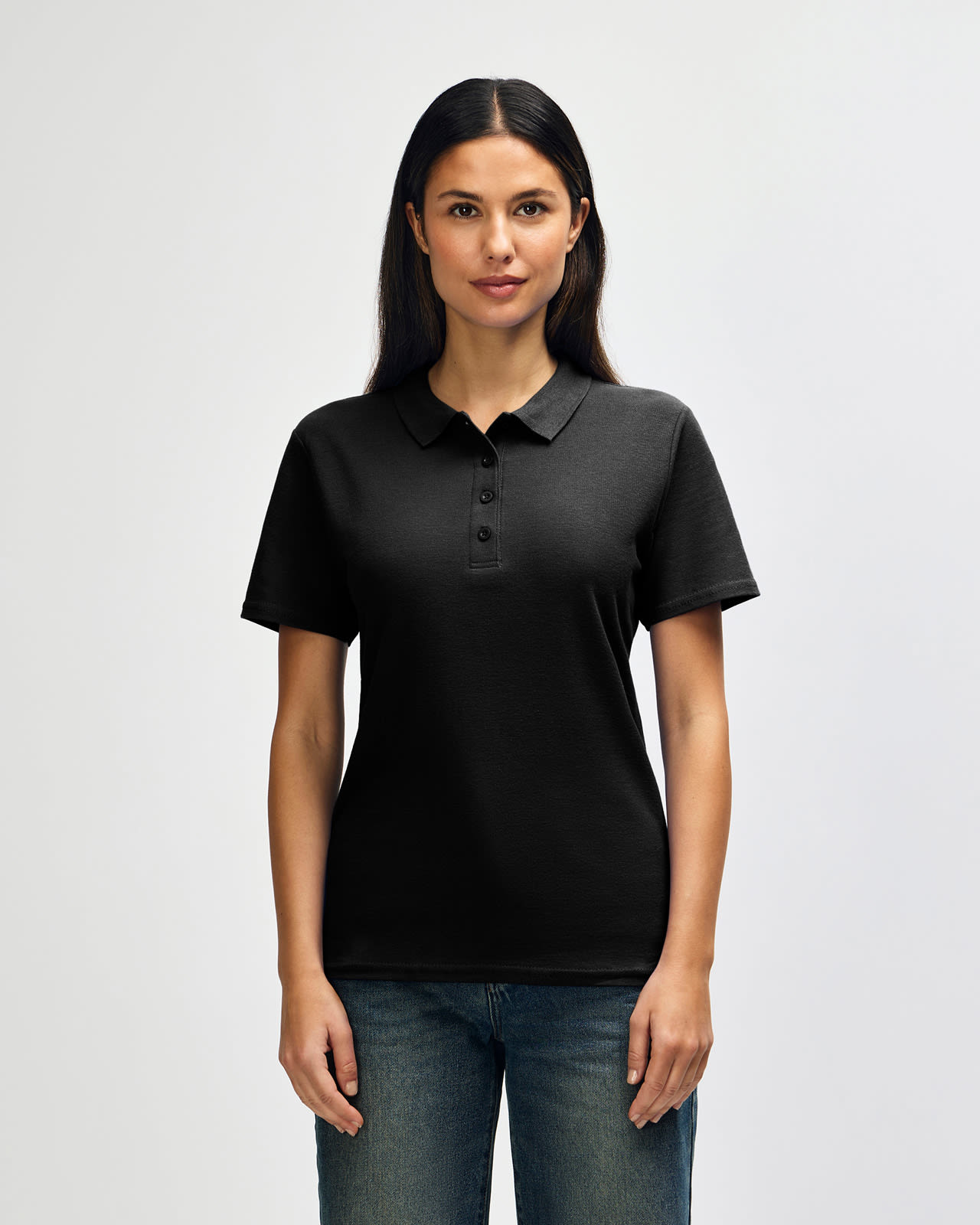 A black Gildan Softstyle ladies' double pique polo shirt with a logo, displayed on a model against a plain background. Gildan Softstyle Ladies' Double Pique Polo - Image 1