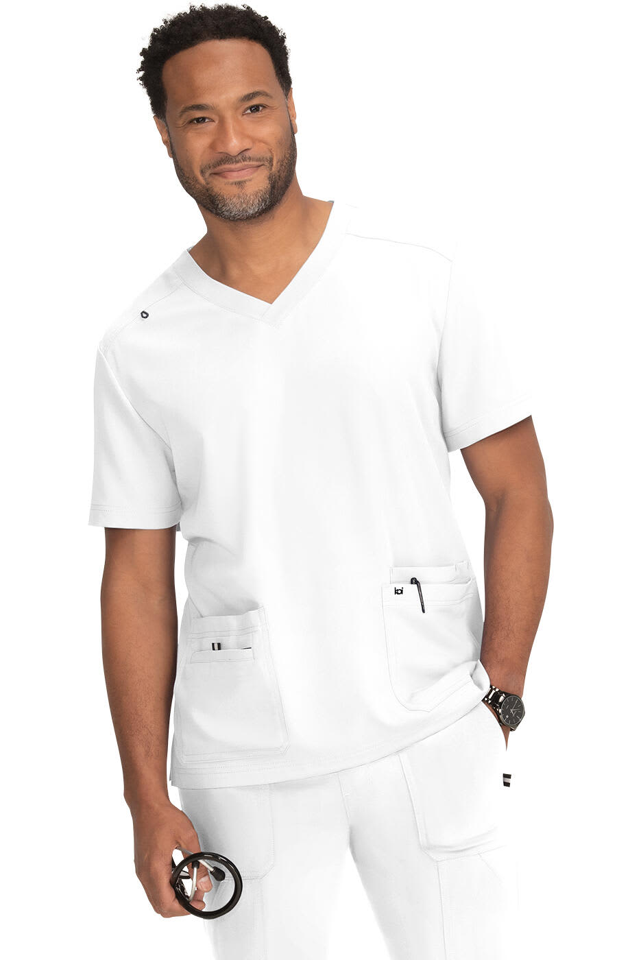 A man in a white scrub top with pockets, smiling and holding a stethoscope, against a neutral background. Free To Be Top - Image 1