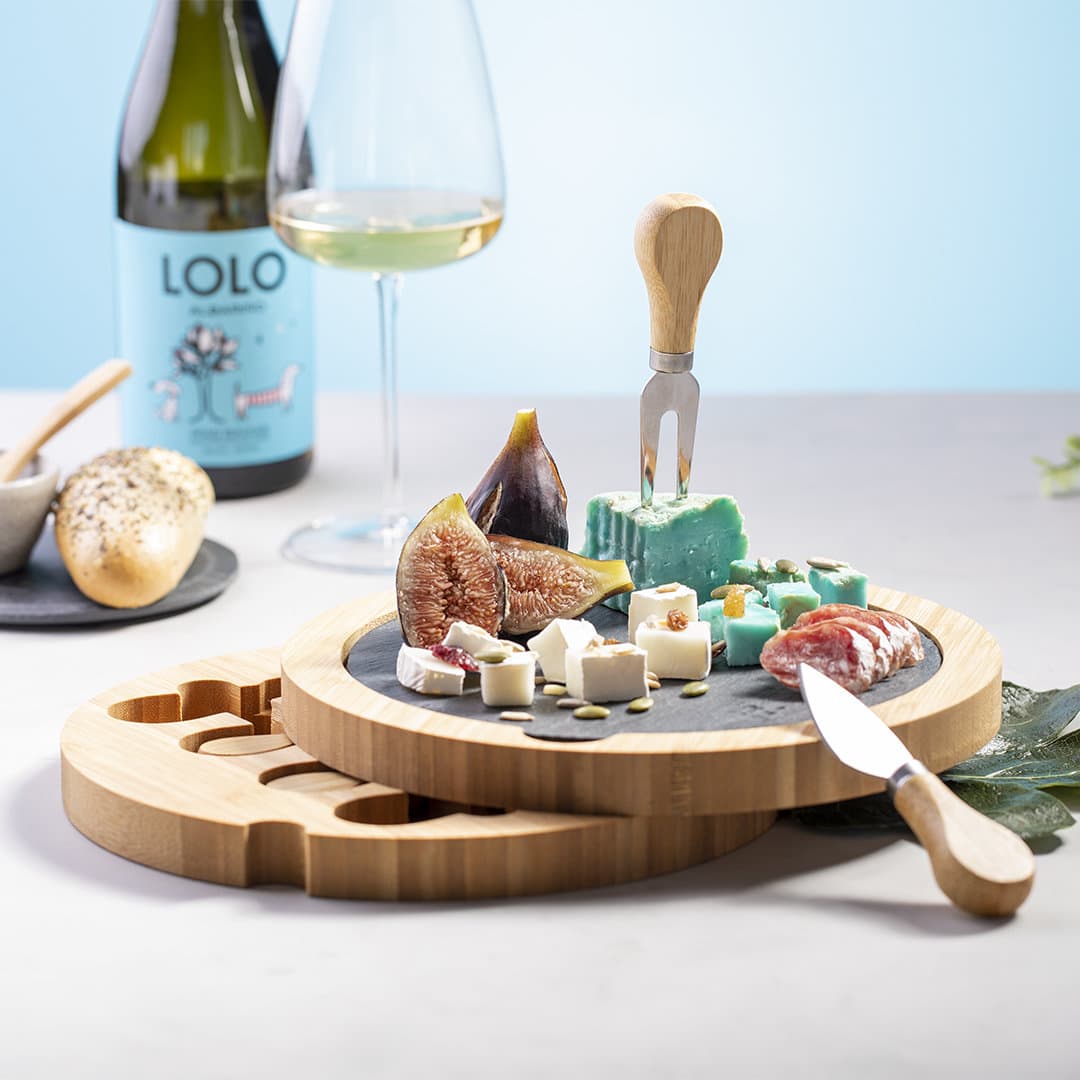 A cheese board featuring assorted cheeses, figs, and salami, with a bamboo base and knife, set against a light background. Pomel - Image 1