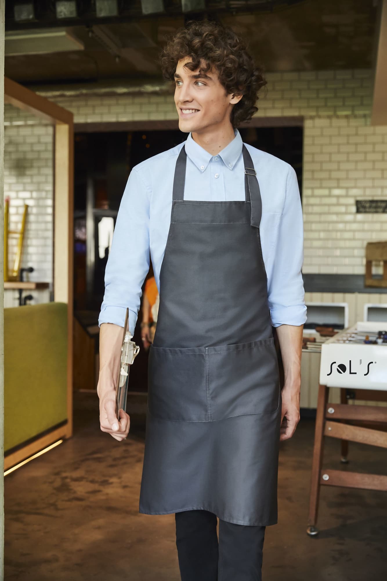 A charcoal grey apron with pockets, made from polycotton, worn by a smiling man in a casual setting. APRON Long WITH POCKETS made from polycotton - Image 1