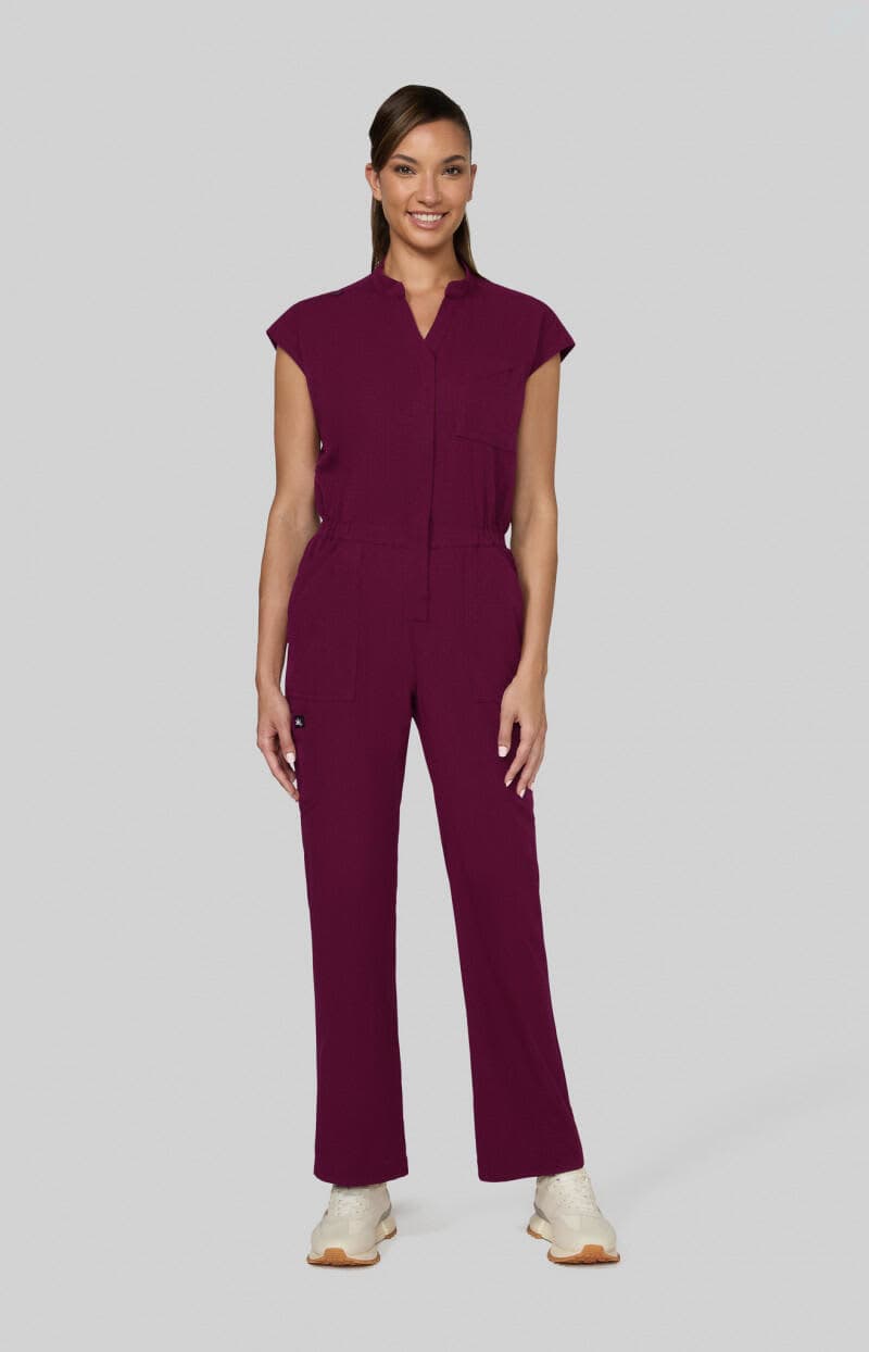 A woman stands in a burgundy jumpsuit with cap sleeves, featuring a front zip and pocket details. Anja Jumpsuit - Image 1
