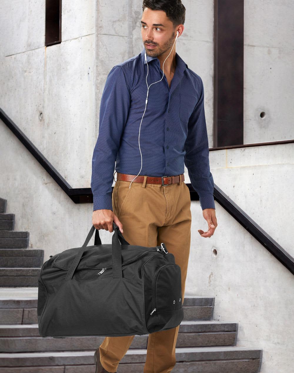 A red duffle bag with a zippered compartment and a pair of shoes resting against it. The bag has a logo. Basic sports bag - Image 1