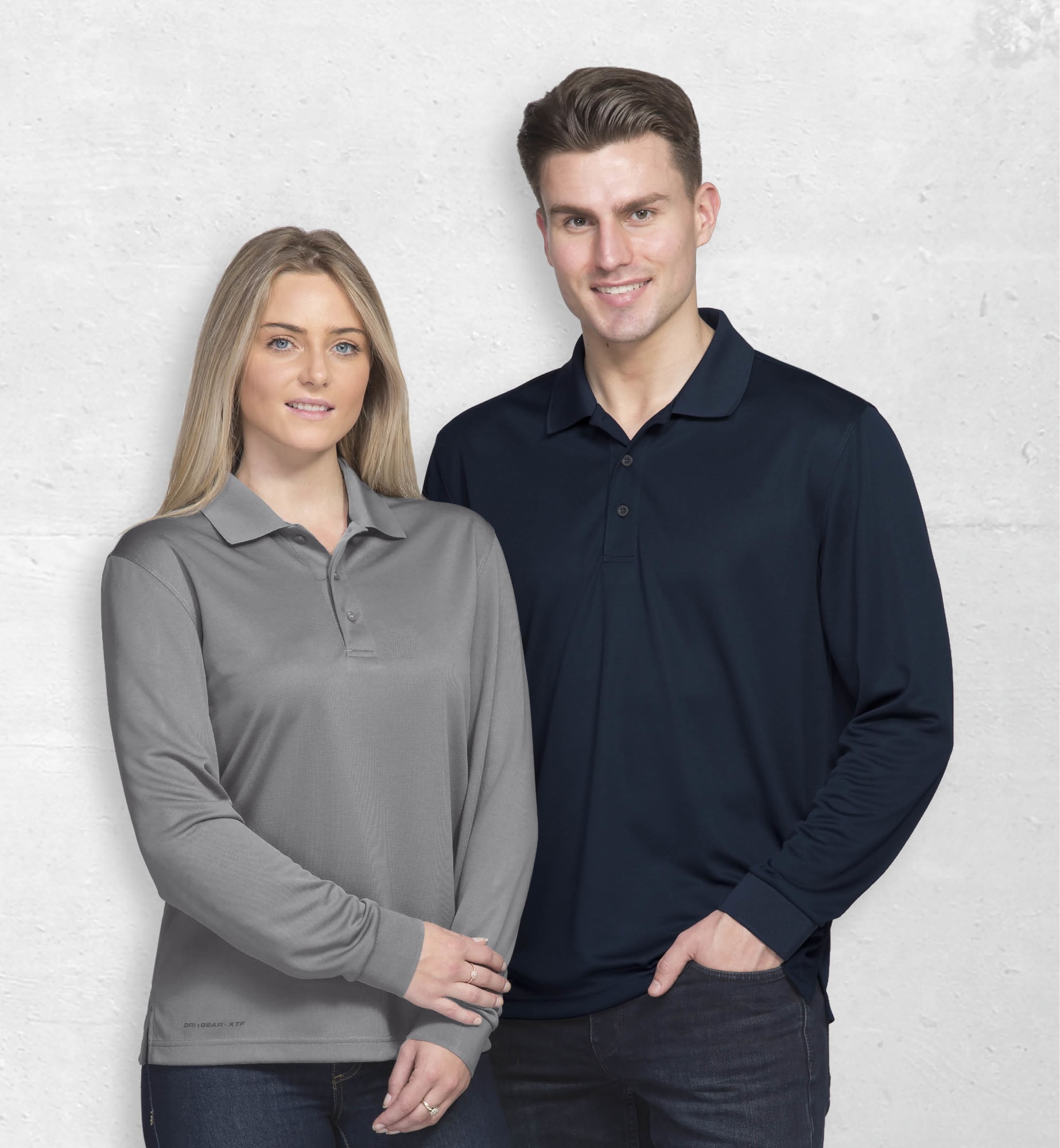A grey long sleeve polo shirt on a woman and a navy long sleeve polo shirt on a man. Both feature branding. Dri Gear Long Sleeve Axis Polo - Image 1