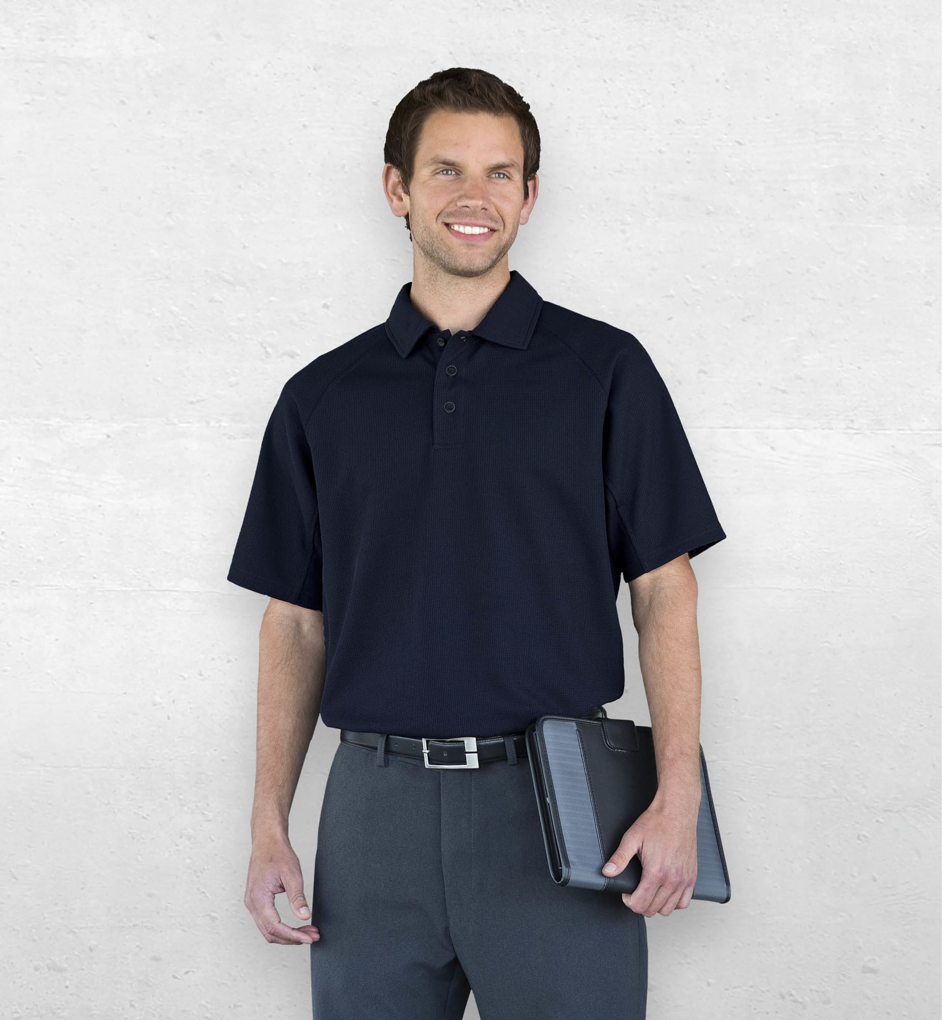 A man wearing a navy Dri Gear Summit Coolmax polo, paired with dark trousers and holding a tablet, stands against a neutral background. Dri Gear Summit Coolmax Polo - Image 1