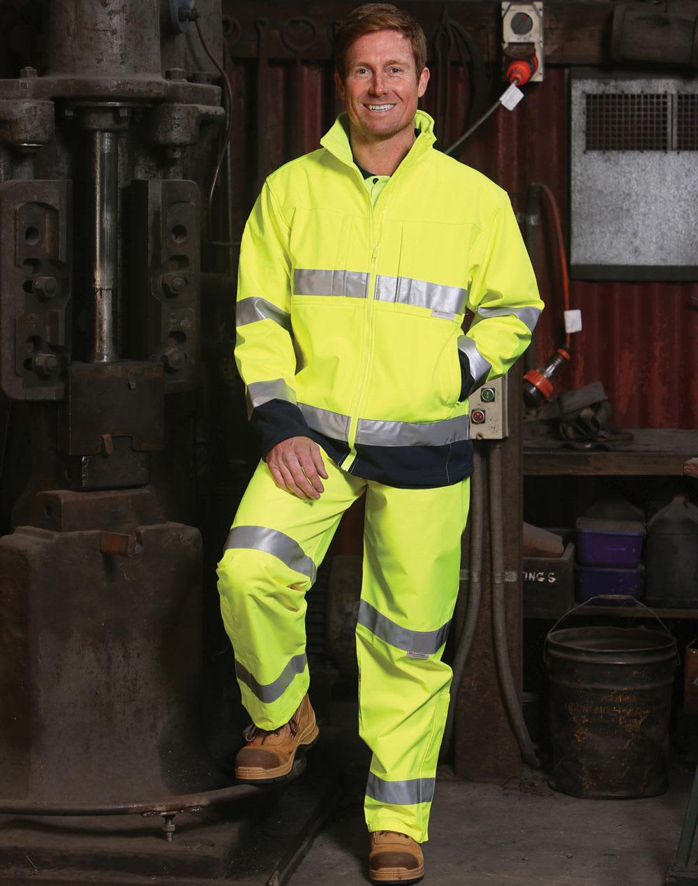 A man stands in a workshop wearing a high-visibility yellow safety pant and jacket with reflective 3M tapes. Hi-Vis 2-tone safety jacket 3M tape - Image 1