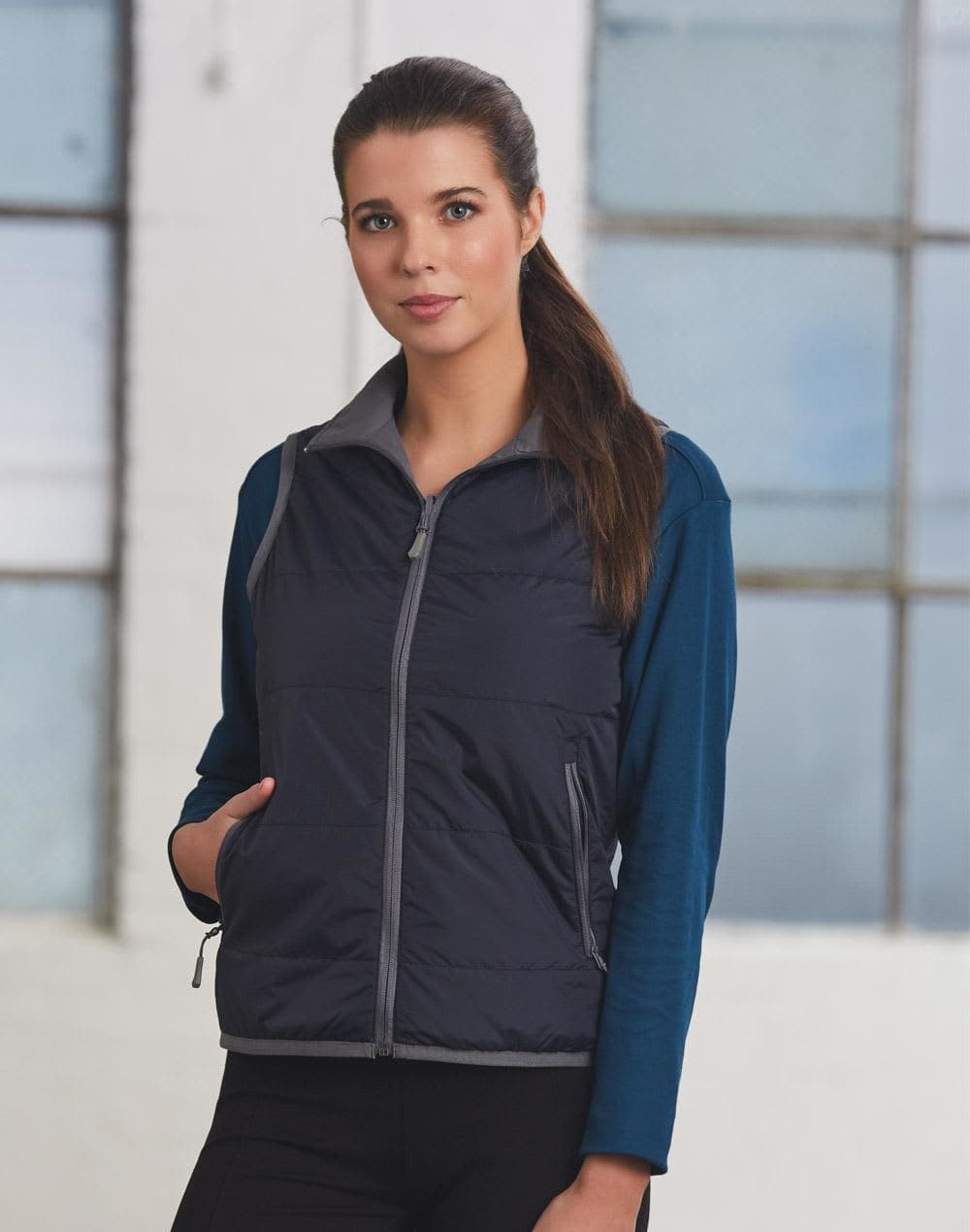 A woman models a navy blue versatile vest with grey accents over a long-sleeve top, featuring pockets and a zip. Ladies' Versatile Vest - Image 1