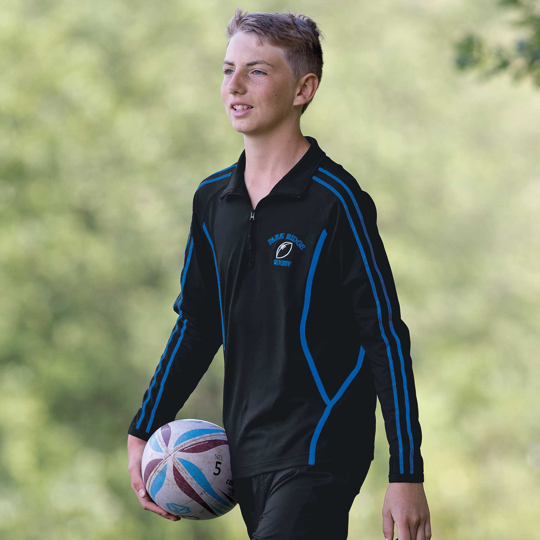 A black pullover with blue accents, featuring a logo, worn by a young athlete holding a rugby ball. Youth Dri Gear Reflex Zip Pullover - Image 1