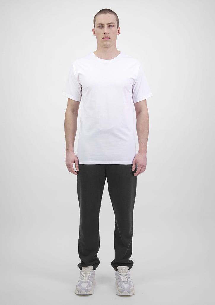 A man stands wearing a plain white t-shirt and black track pants. The track pants feature a logo. Mens Basis Track Pant - Image 1