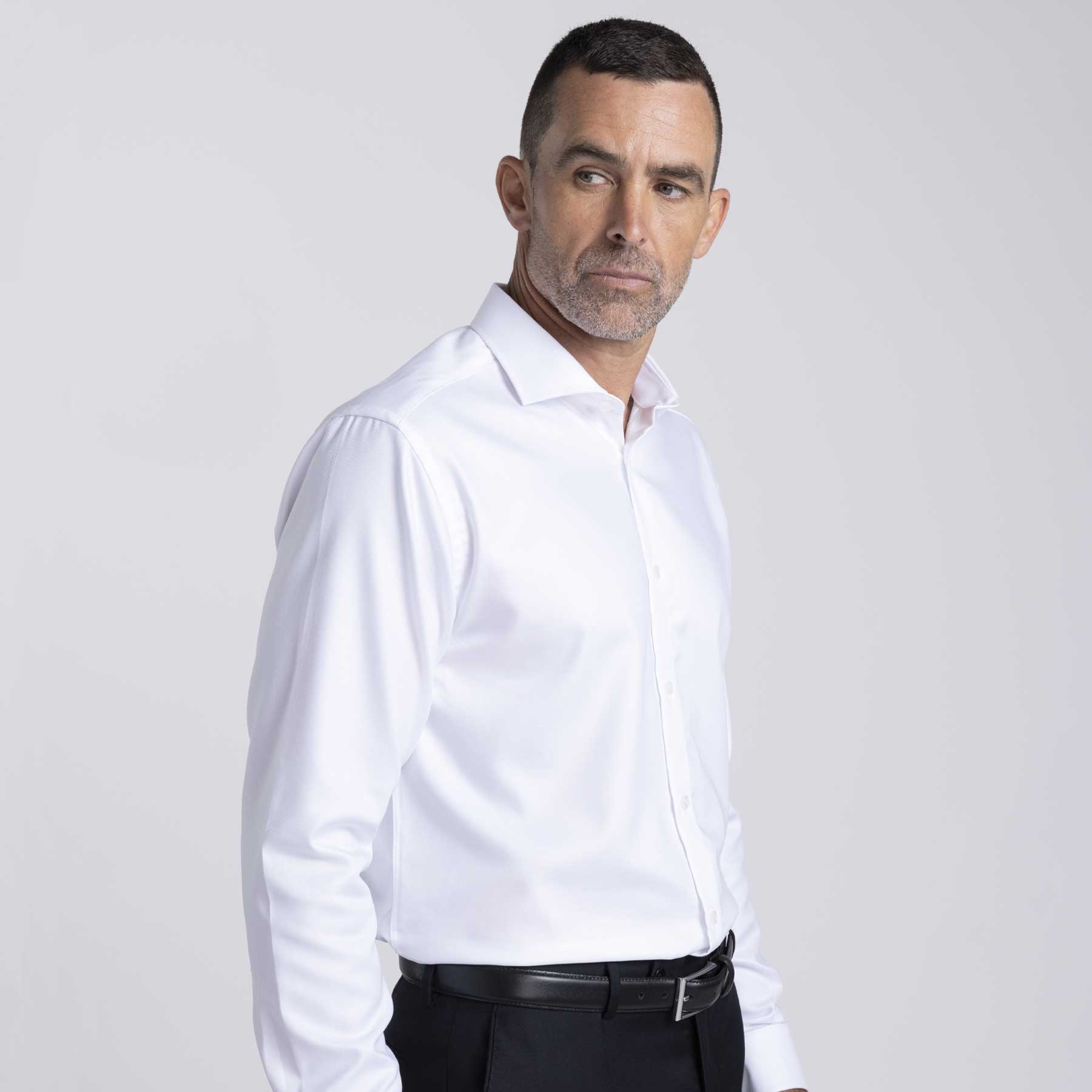 A white button-up shirt on a male model, featuring a collar and a logo. The model wears black trousers. Barkers Corporate Origin Shirt – Mens - Image 1