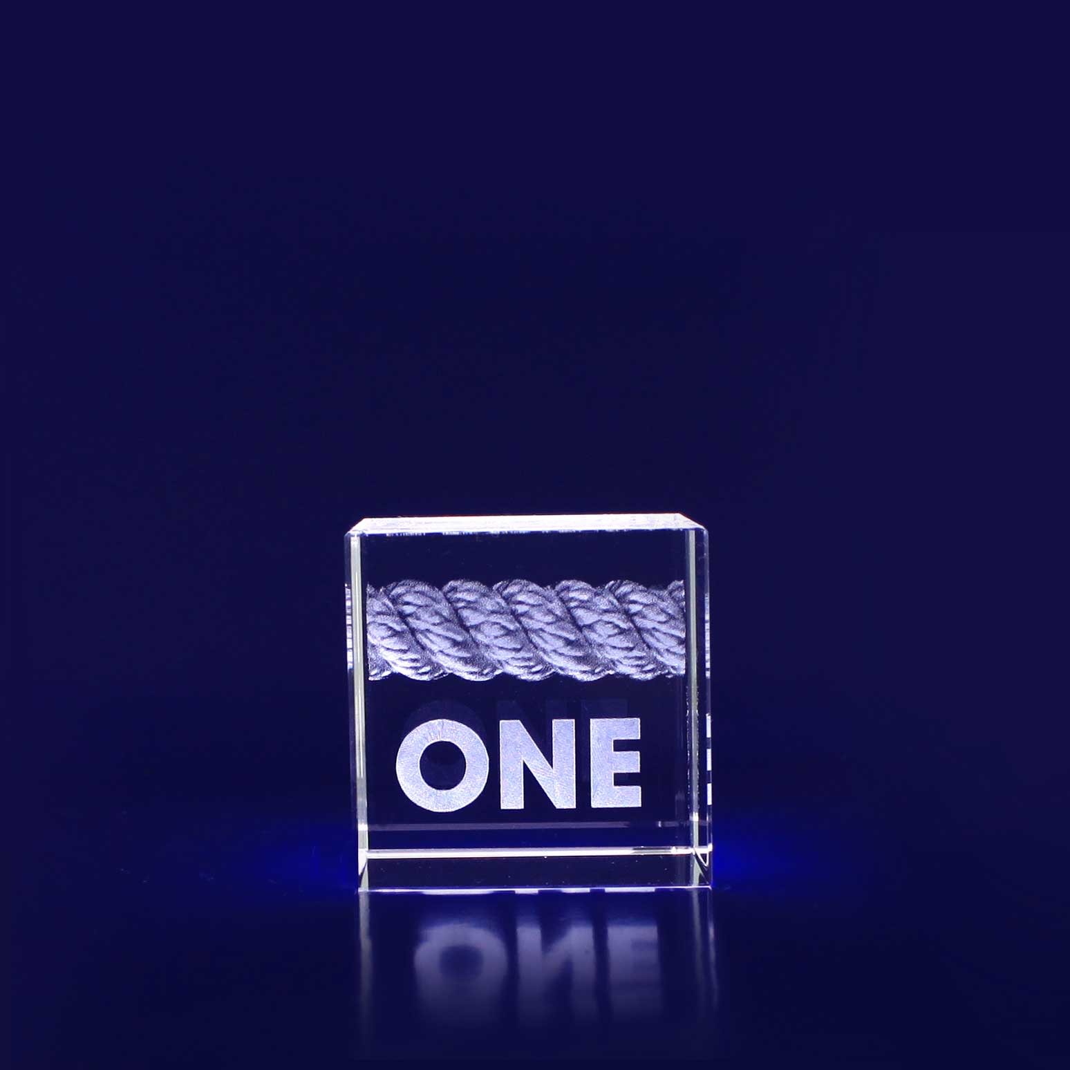 A 3D crystal cube with a rope design inside, featuring the word "ONE" in bold lettering. The cube is clear and surrounded by a deep blue background. 3D Crystal Cube (40mm) - Image 1