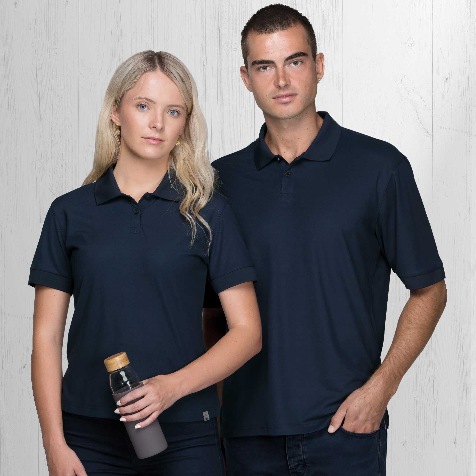 Two models wearing navy blue Dri Gear Renew Eco Polo shirts, one holding a drink bottle, against a light wooden background. Dri Gear Renew Eco Polo – Mens - Image 1