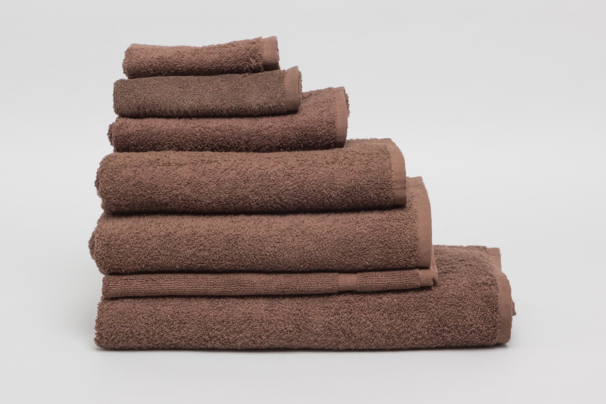 A stack of chocolate brown towels in various sizes with a textured finish, featuring a logo. Elite Small Hand Towel 500 gsm Chocolate - Image 1
