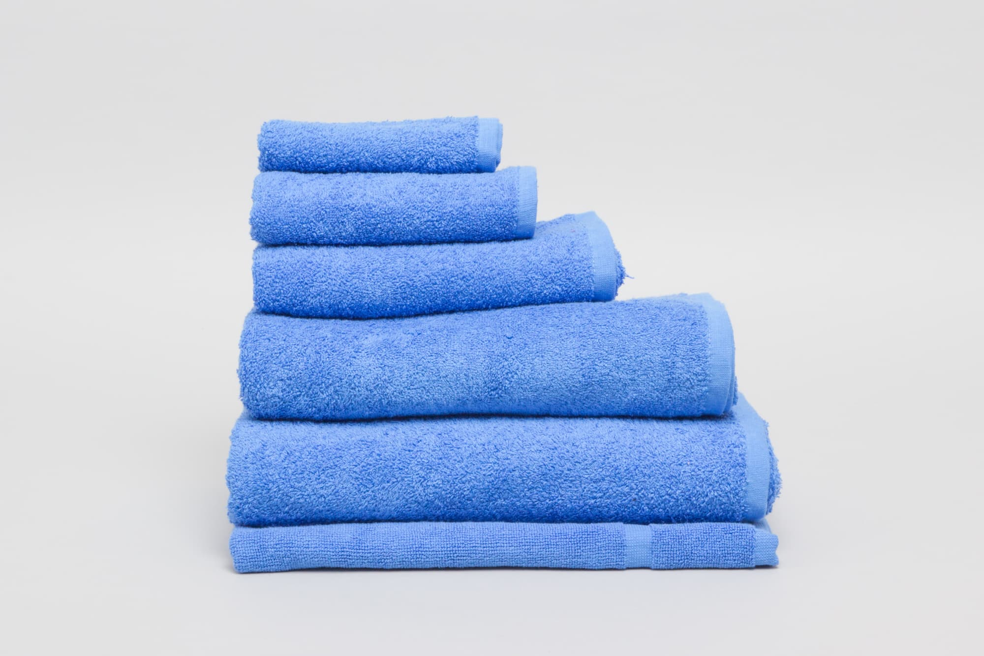 A stack of light blue towels in varying sizes, featuring a soft, textured surface. The image includes a logo. Elite Small Hand Towel 500 gsm Royal - Image 1