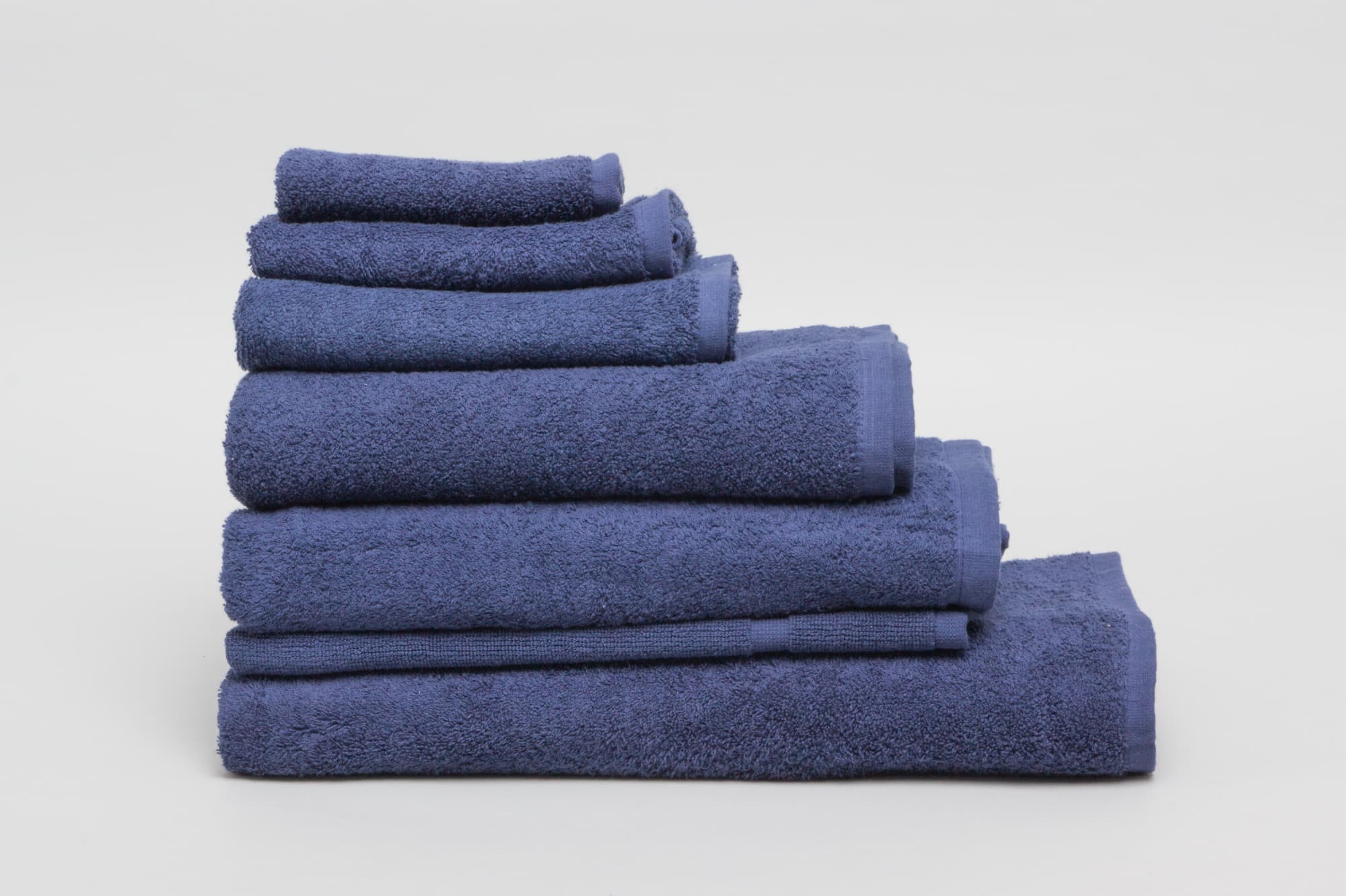 A stack of navy towels in various sizes, featuring a soft texture and a neat presentation. Elite Large Hand Towel 500 gsm Navy - Image 1
