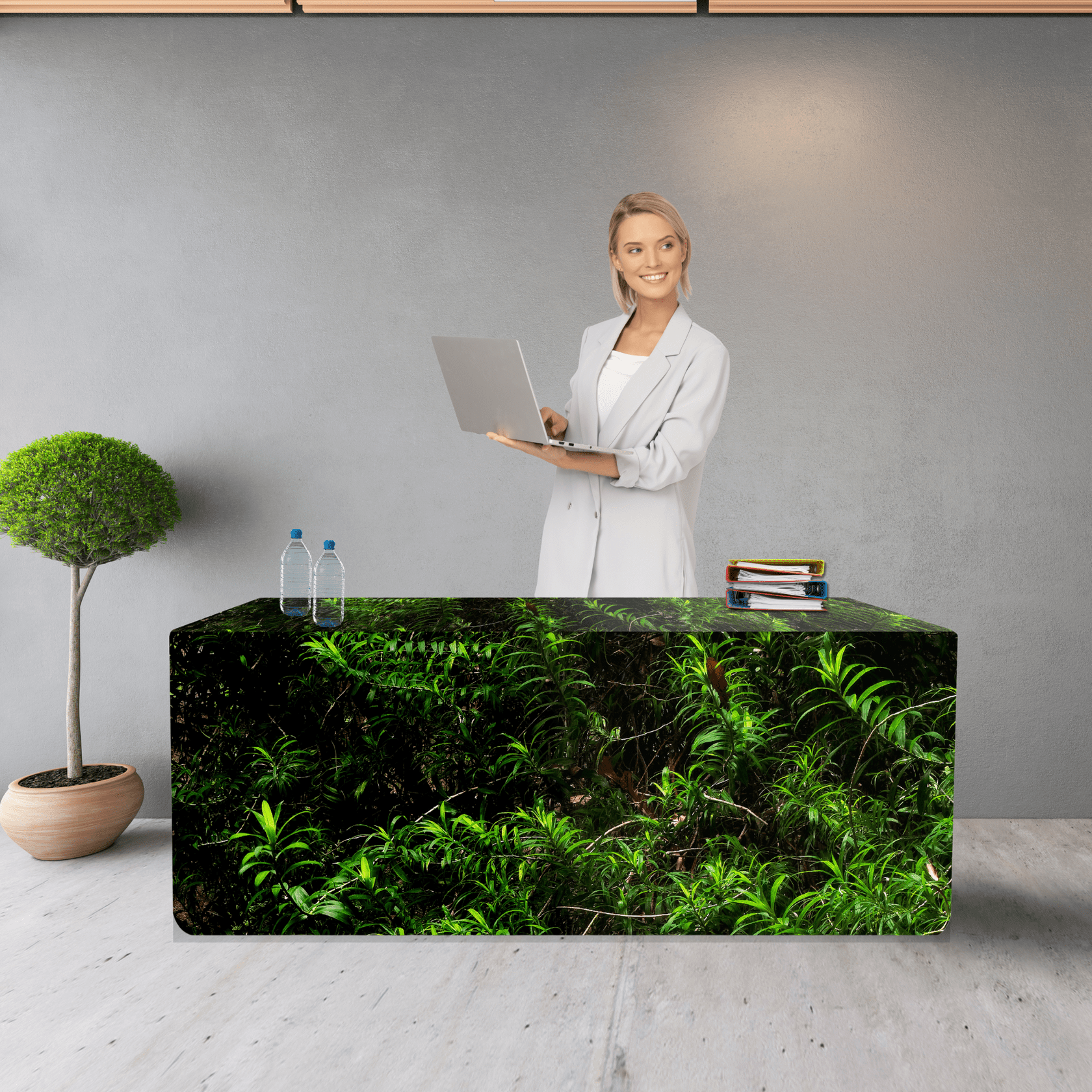 A fitted table cover featuring a green foliage design, with a woman standing behind a table, laptop in hand. rPET Fitted Table Cover 4ft (1200mm) - Image 1