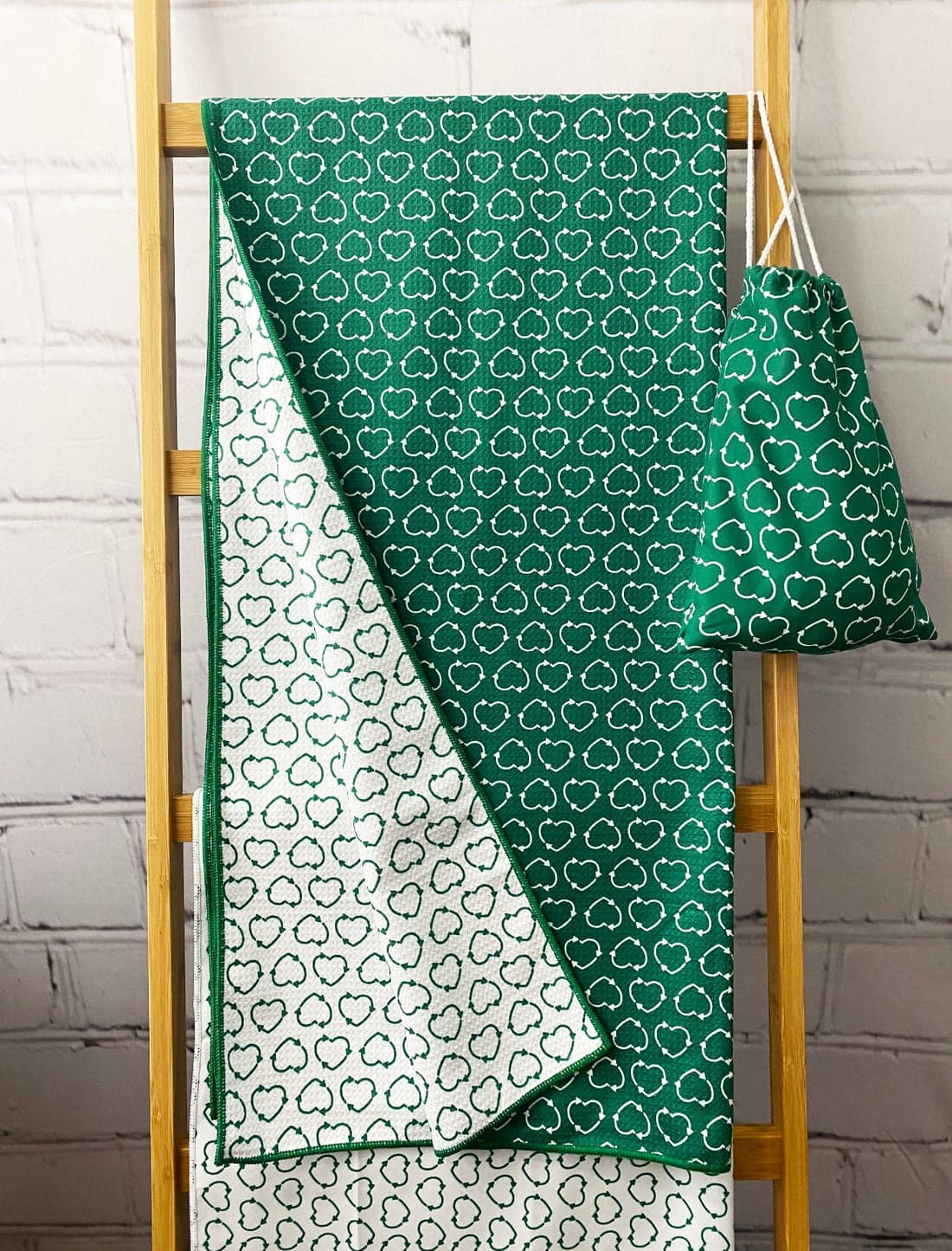 A green beach towel with a cloud pattern, displayed on a wooden rack alongside a matching carry pouch. rPET Sand Free Beach Towel - Image 1