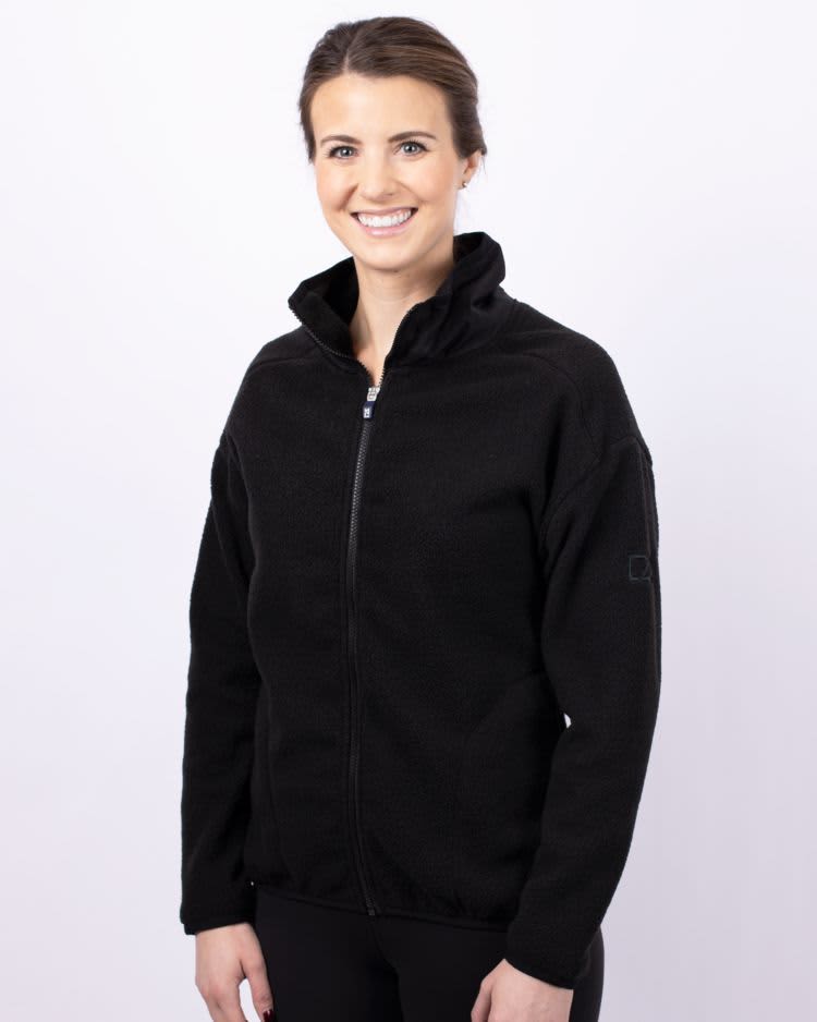A woman wearing a black eco Sherpa jacket with a zip-up front and a stand collar. The jacket has a logo on the sleeve. Ladies Cascade Eco Sherpa Jacket - Image 1