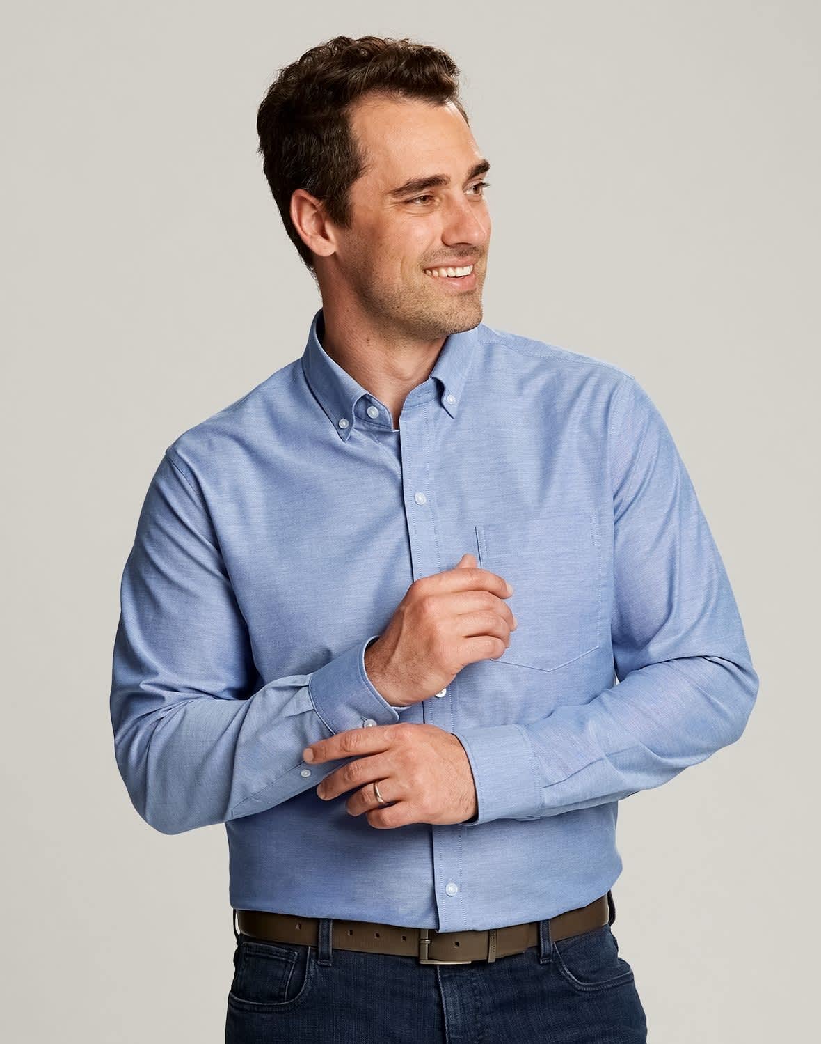 A light blue button-up shirt is worn by a smiling man. The shirt features a collar and has a logo. CB Men's Stretch Oxford - Image 1