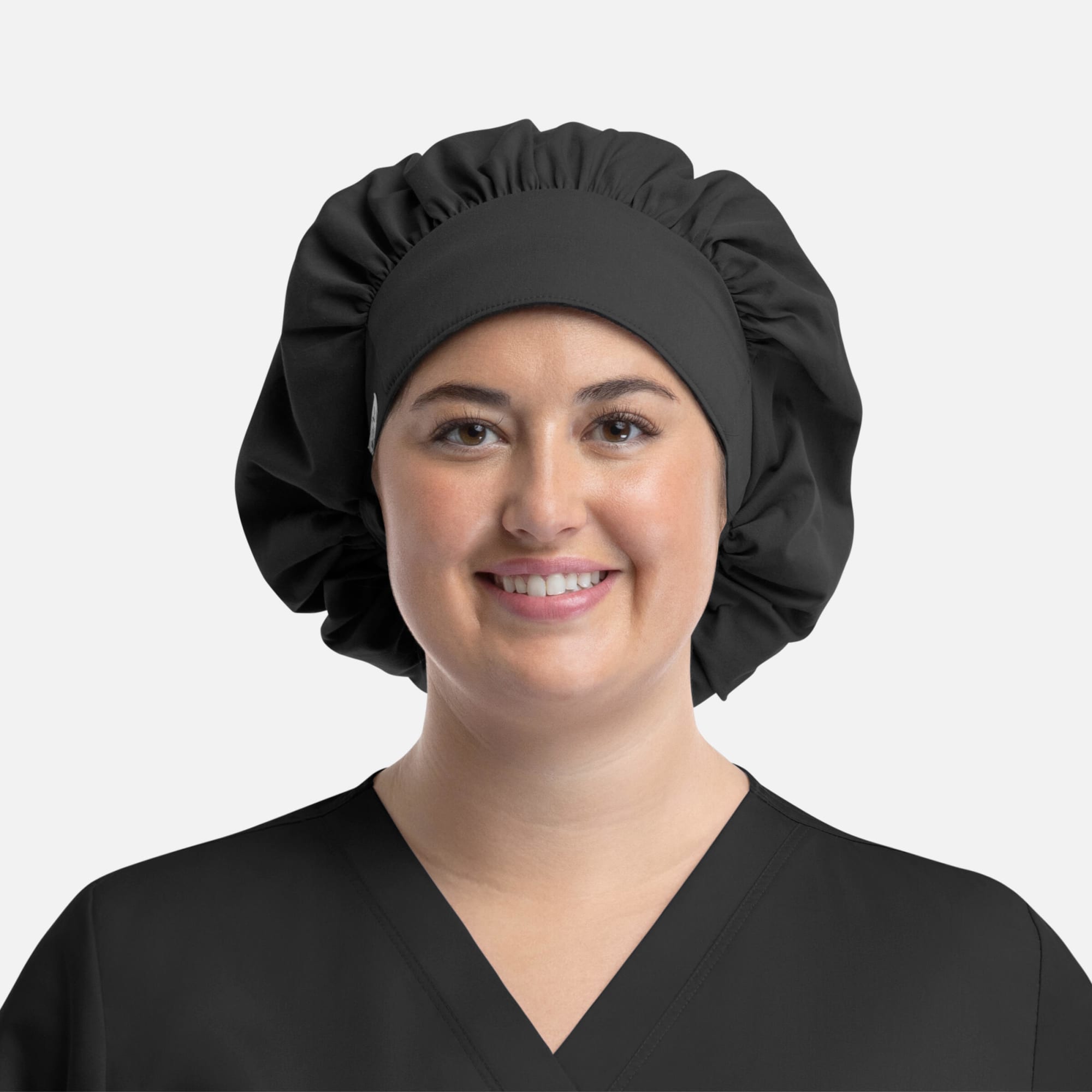 A black bouffant cap worn by a smiling person in a black top. The cap features a gathered design and a smooth band. Bouffant Cap - Image 1