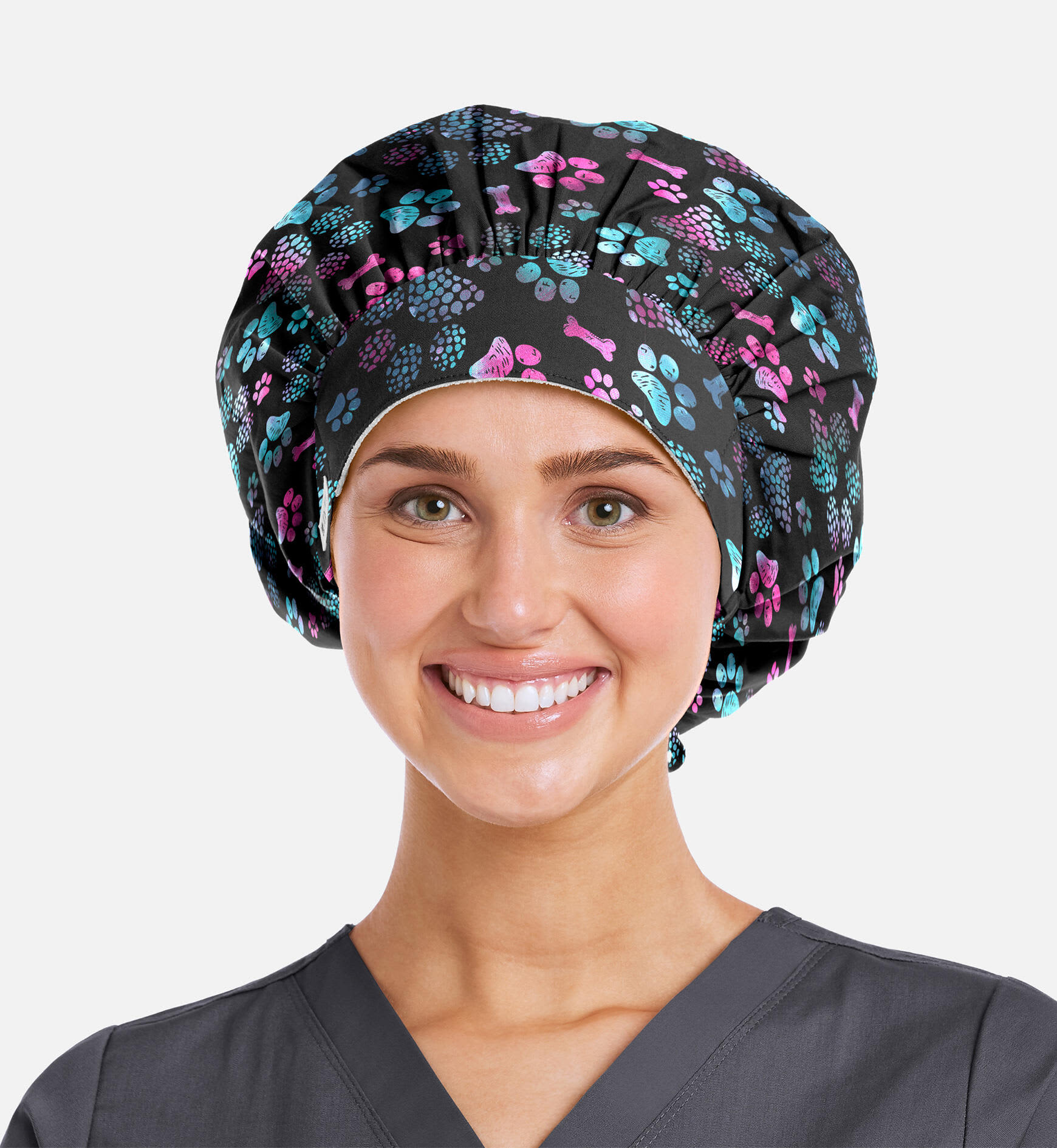 A bouffant cap featuring a black background with colourful floral and paw print patterns. The model is smiling. Printed Unisex Bouffant Cap - Image 1