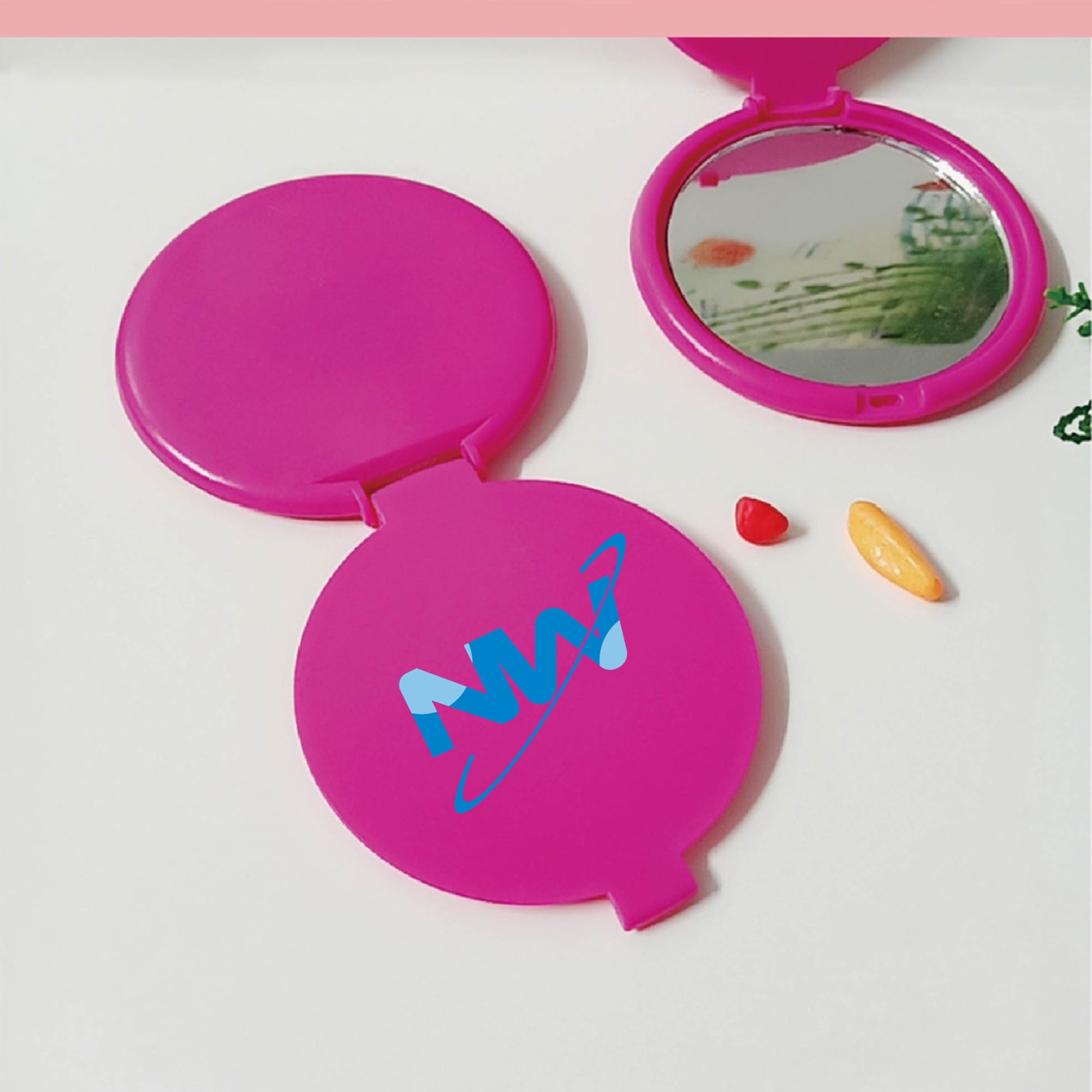 A round, pink folding mirror with a reflective surface and a logo on the outer casing. Round Folding Single-sided Mirror - Image 1
