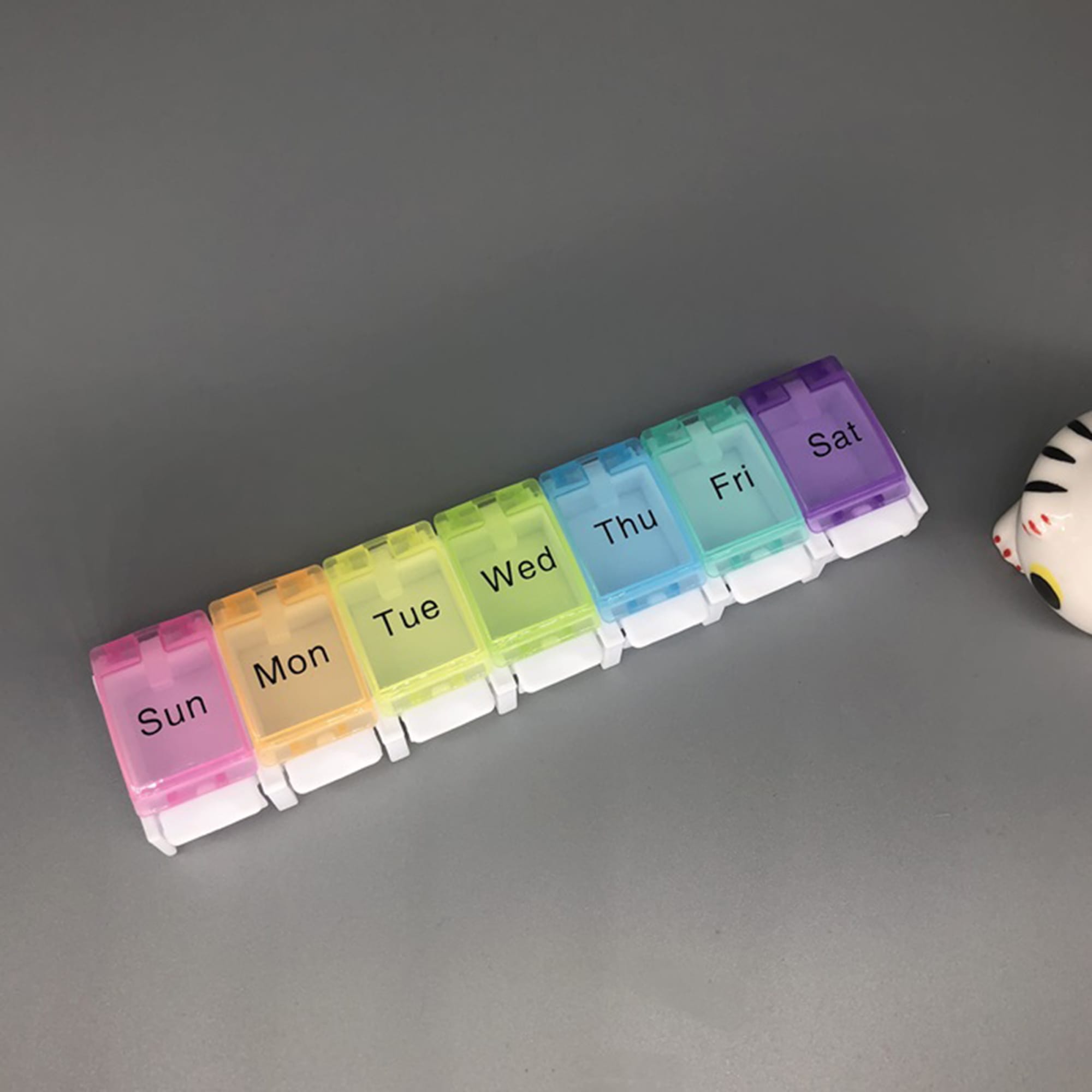 A multi-coloured seven-grid pill box featuring compartments for each day of the week. It has a white base and a logo. One Week / 7 Grid Pill Box - Image 1