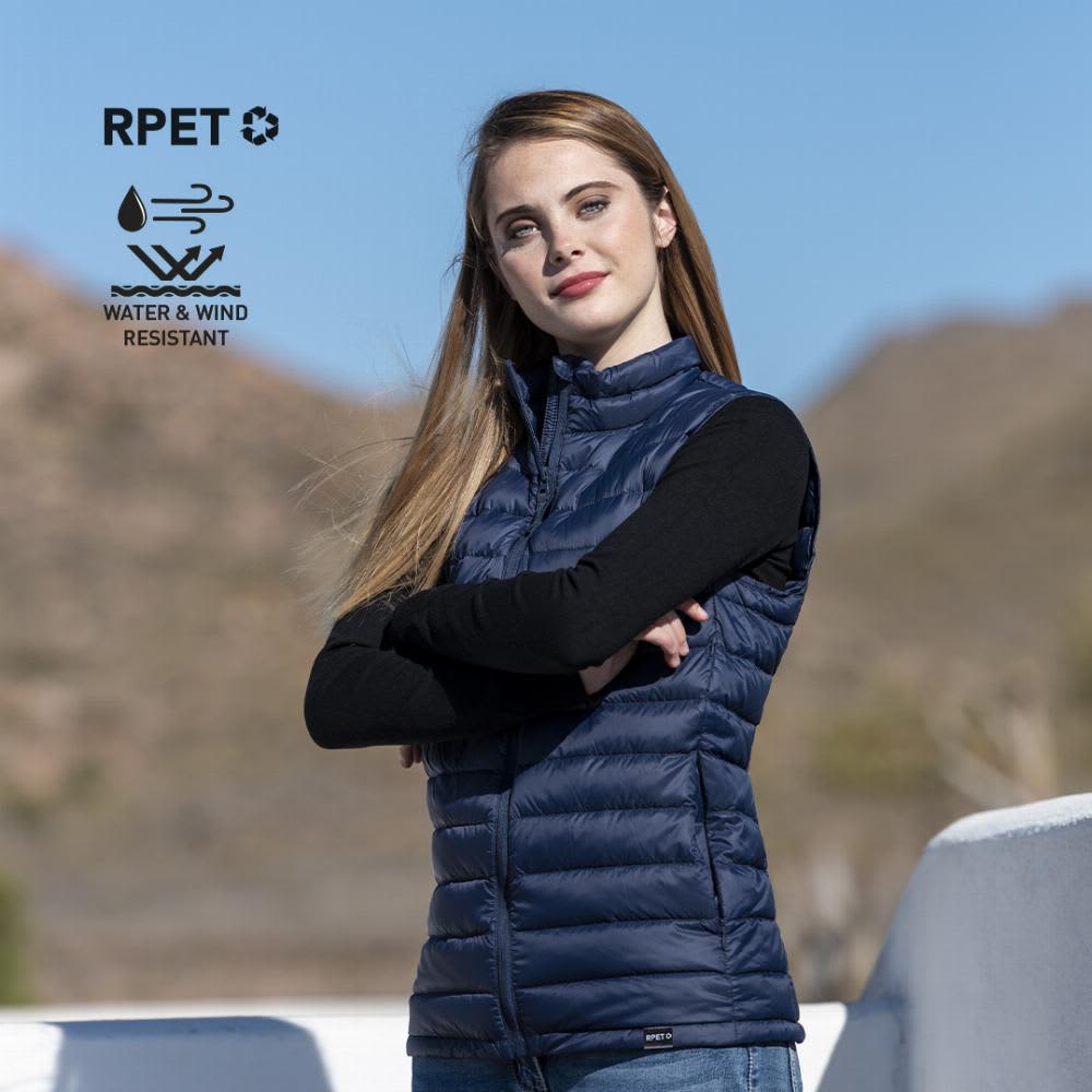 A model wearing a navy blue sleeveless puffer vest against a mountain backdrop, featuring a logo for eco-friendly materials. Rostol - Image 1