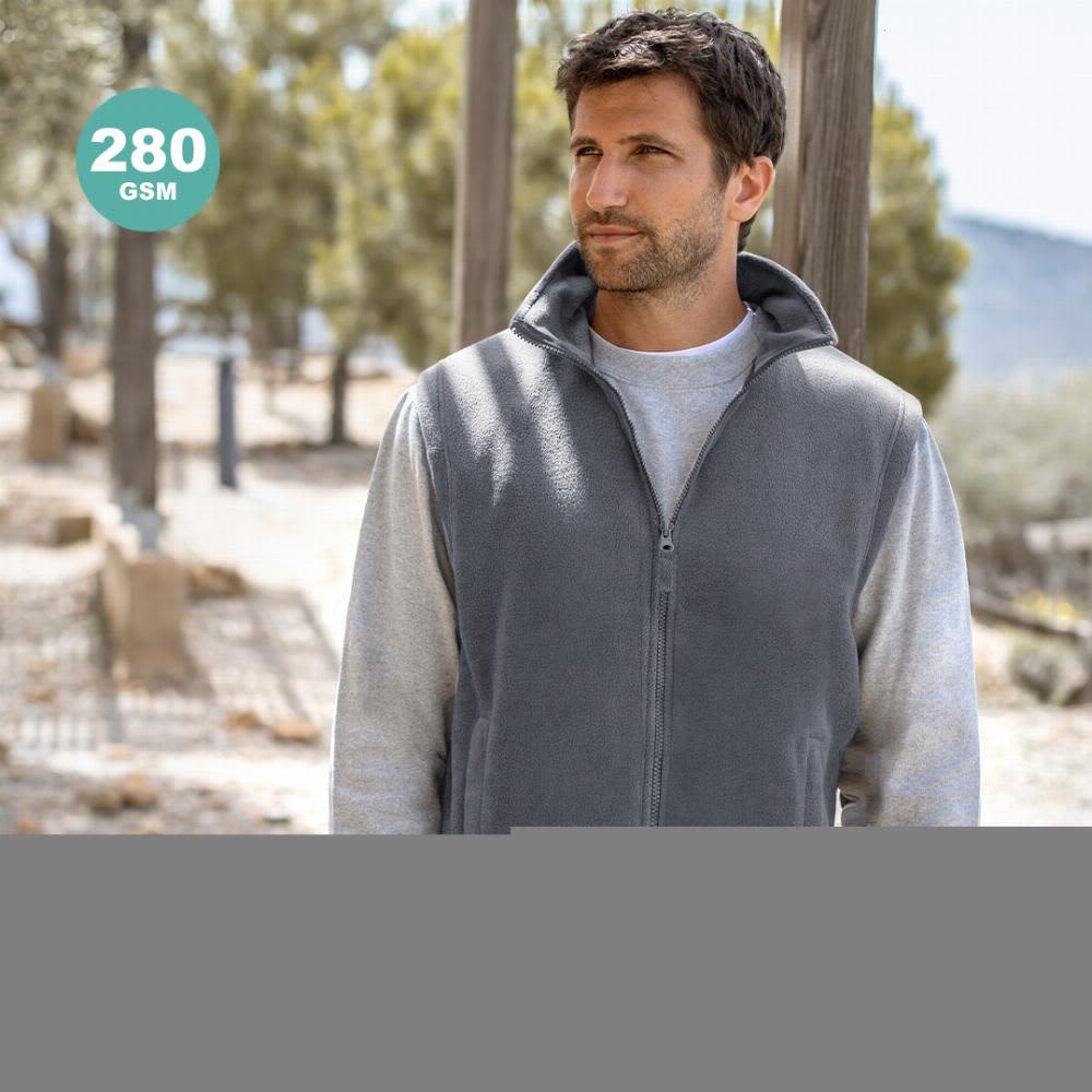 A man wearing a grey vest over a light-coloured long-sleeve shirt, standing outdoors among trees. The vest has a logo. Destin - Image 1
