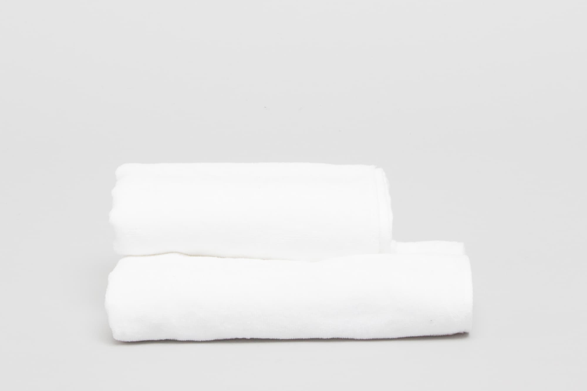 Two neatly rolled white hand towels on a light grey background. The towels have a soft texture and a logo. Signature Hand Towel 380 gsm White - Image 1