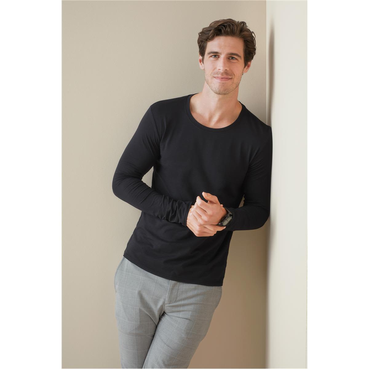 A black long sleeve shirt displayed on a man leaning against a wall, paired with light-coloured pants. Men's Clive Long Sleeve - Image 1