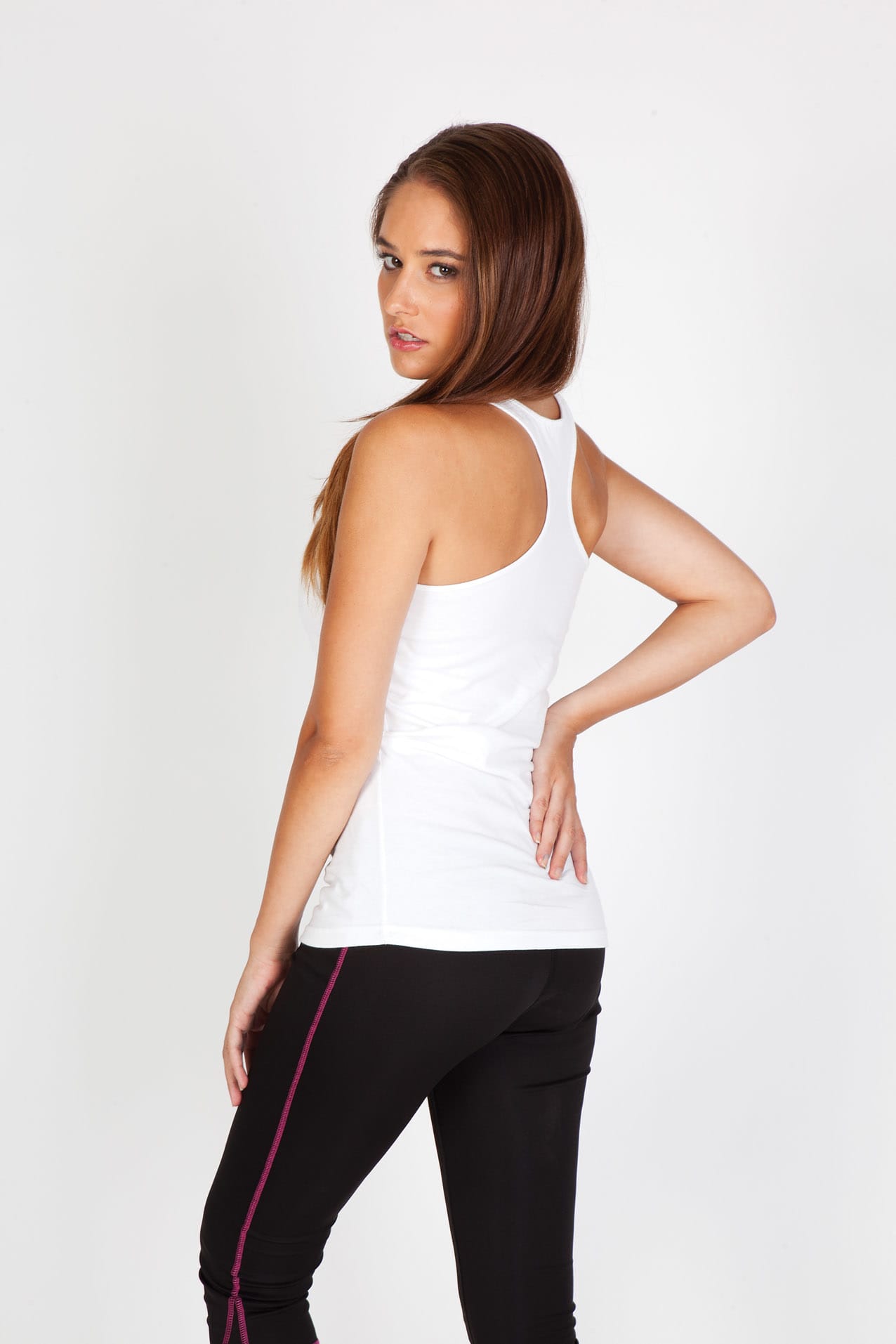 A white women's T-back singlet is displayed, featuring a fitted design and a model wearing it with black pants. Womens Tback Singlet - Image 1