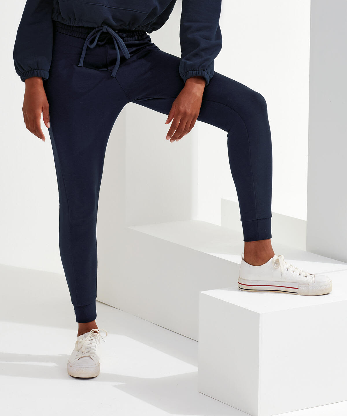 Fitted joggers in navy blue with a drawstring waist. A stylish and comfortable fit. White sneakers complement the look. Fitted Joggers - Image 1
