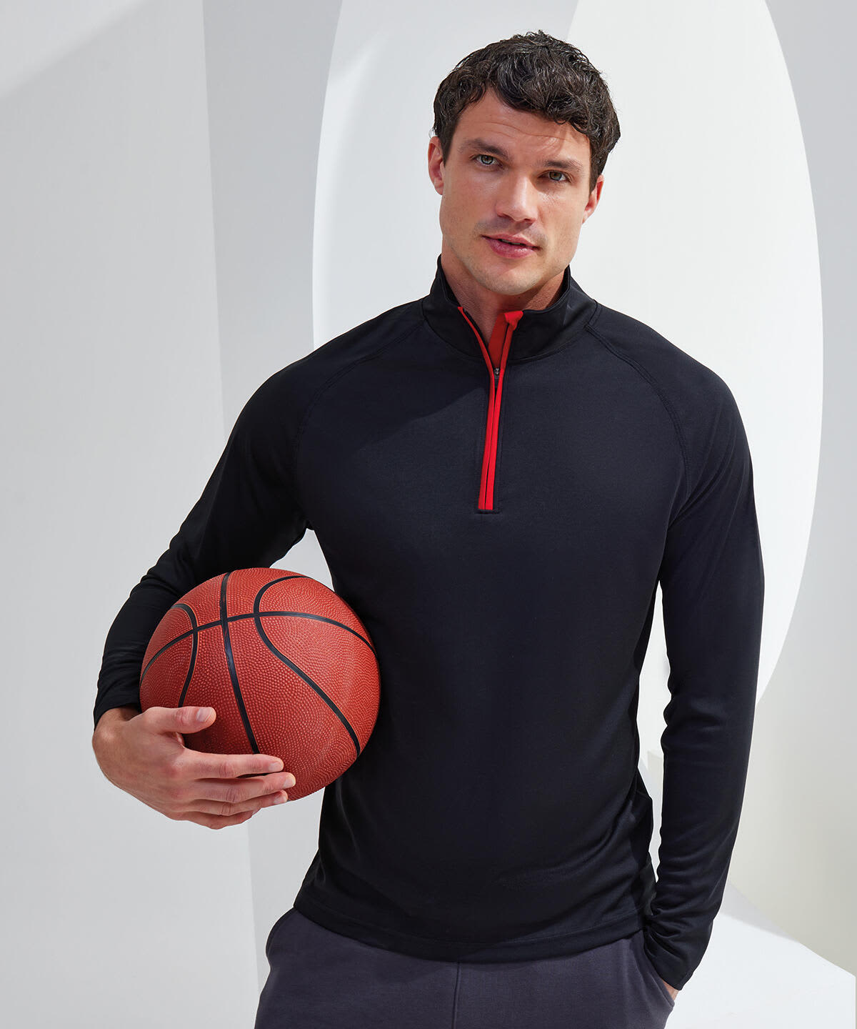 A model wearing a black long sleeve performance 1/4 zip top with a red zip, holding a basketball. Long Sleeve Performance 1/4 Zip - Image 1