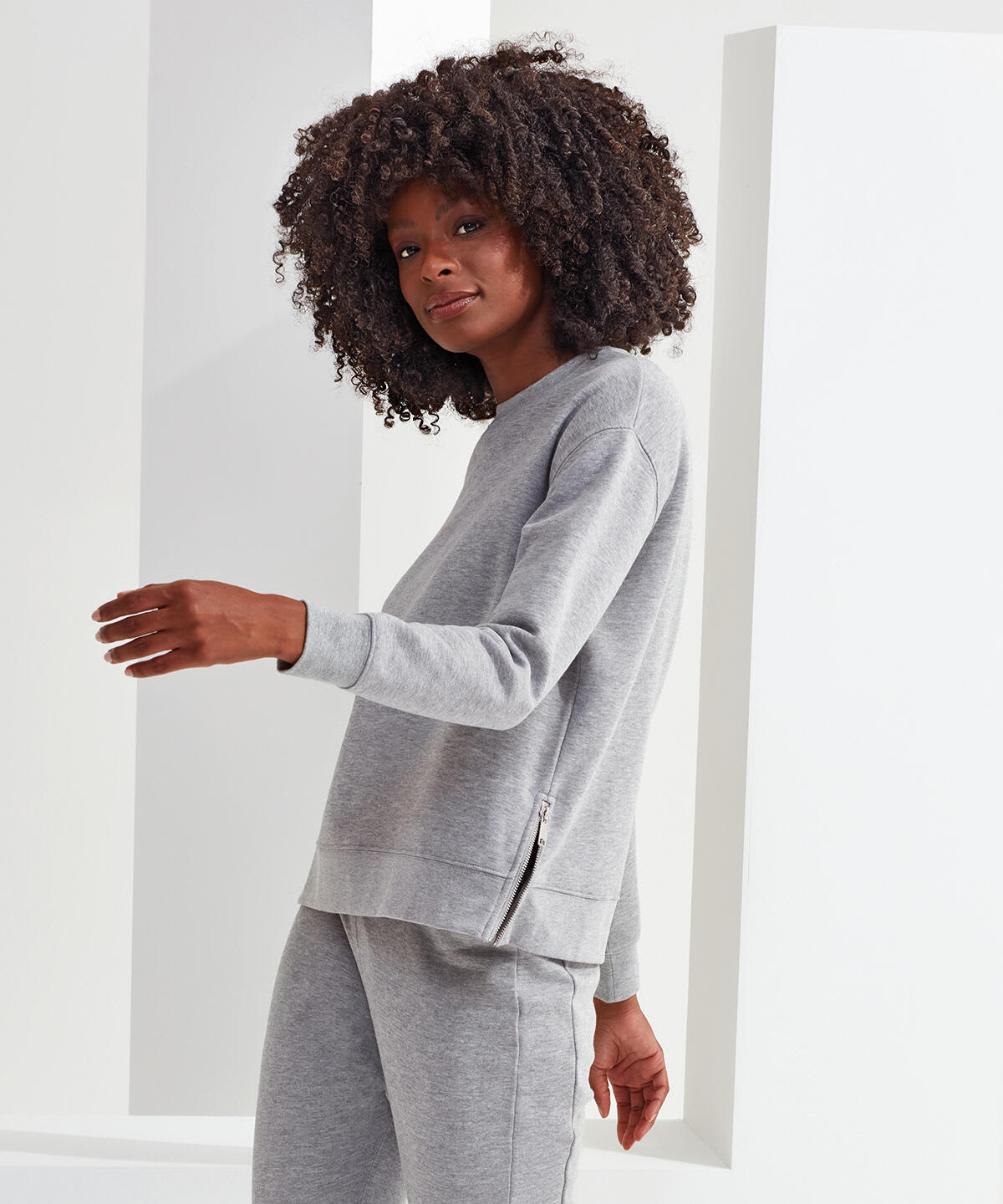 A grey sweatshirt featuring a zip detail, shown on a model with curly hair, against a minimalist background. Recycled Chill Zip Sweatshirt - Image 1