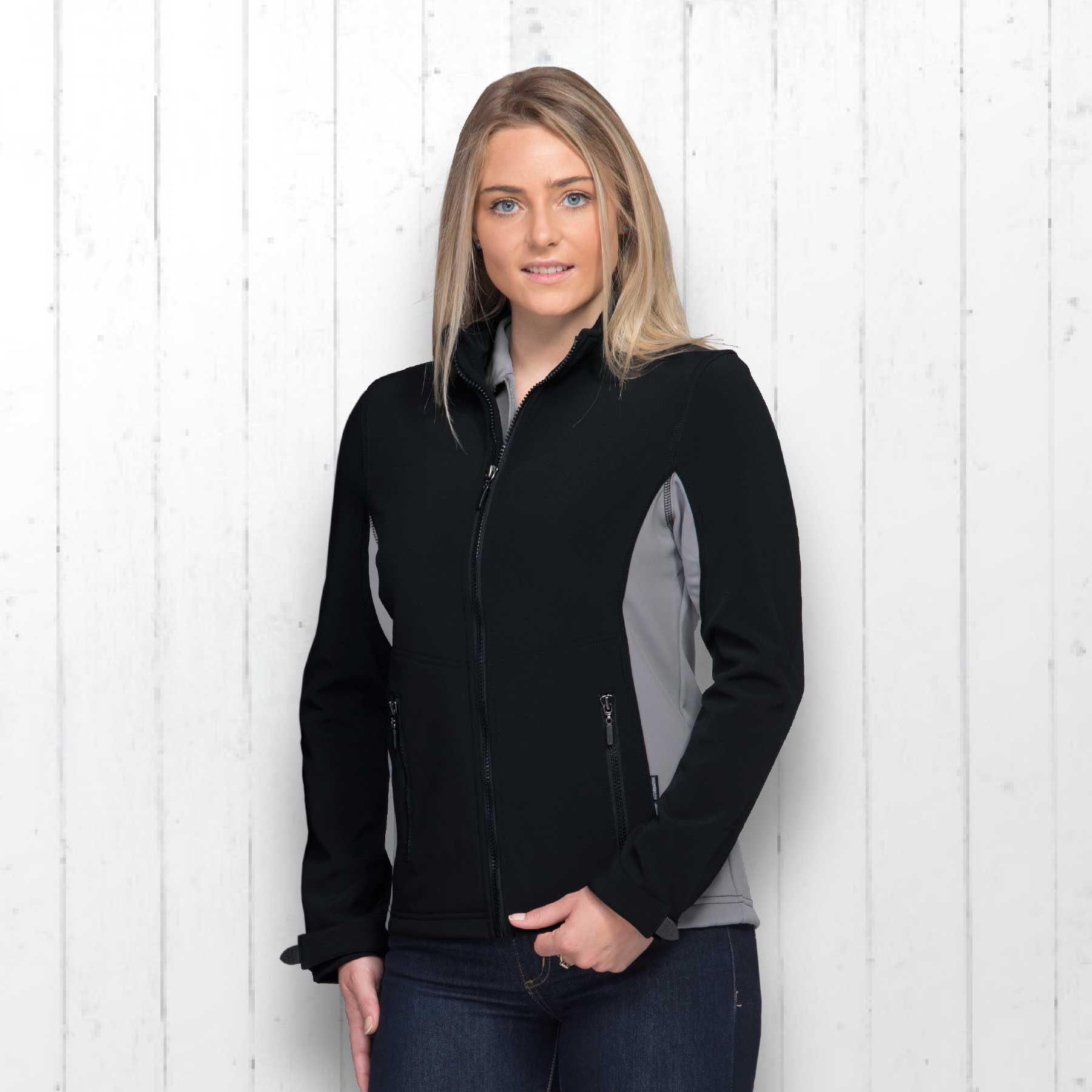 A woman models a black and grey soft shell jacket with zip pockets and a logo on the chest. X-Trail Jacket - Womens - Image 1