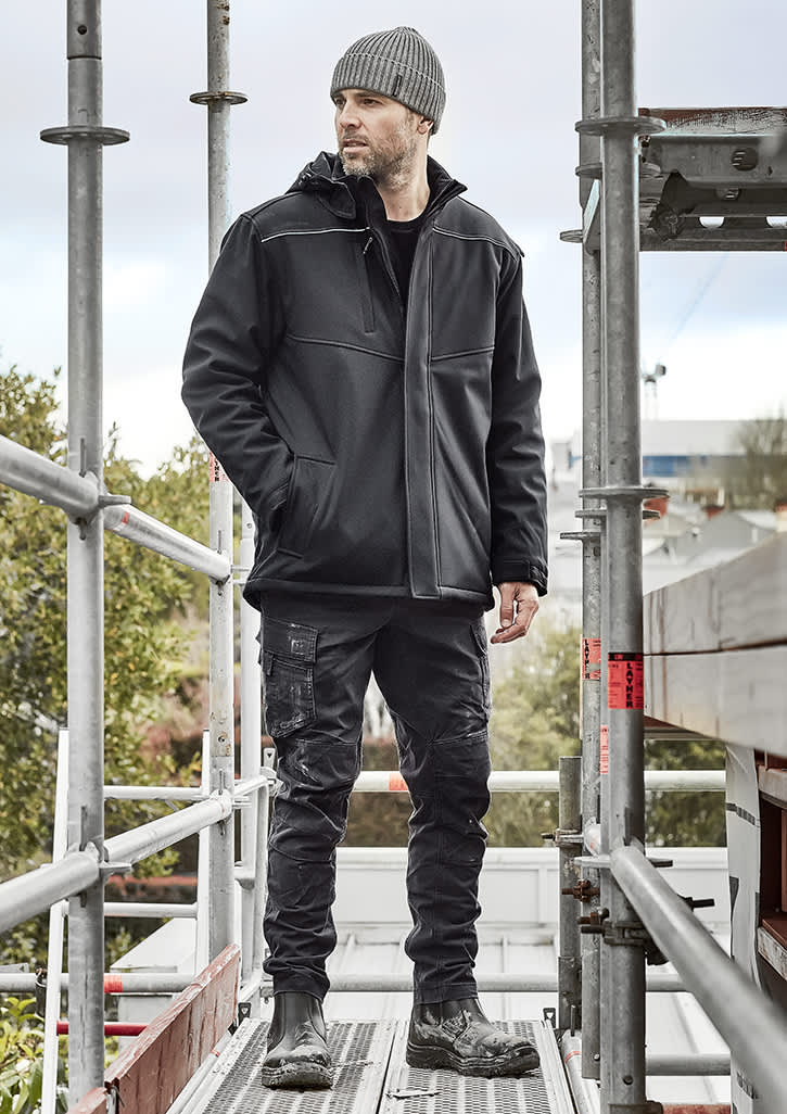 A man wearing a black unisex softshell jacket stands on scaffolding, paired with black trousers and boots. Unisex Antarctic Softshell Jacket - Image 1